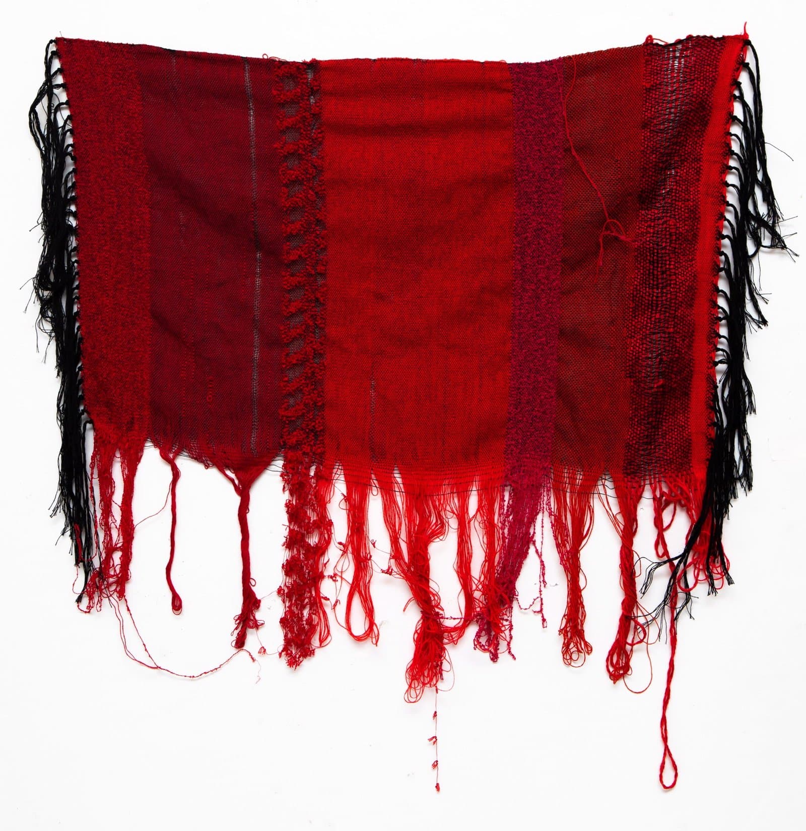 Woven textile in deep red with black and white striped fringe along the sides and long red fringe at bottom.