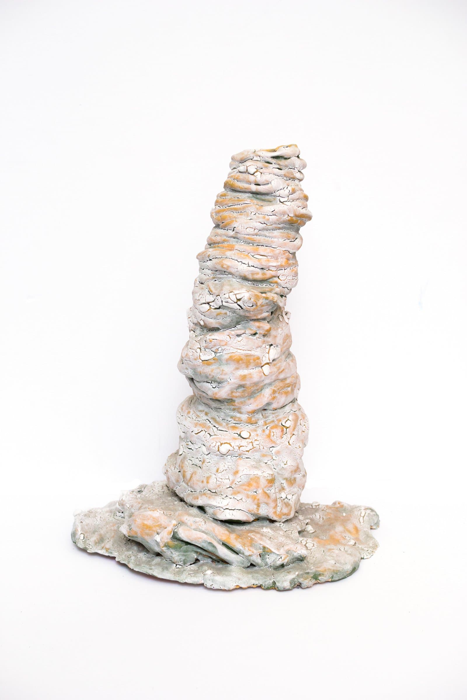 Tall ceramic sculpture resembling a stacked rock formation with crackled white and orange glaze on a flat irregular base.