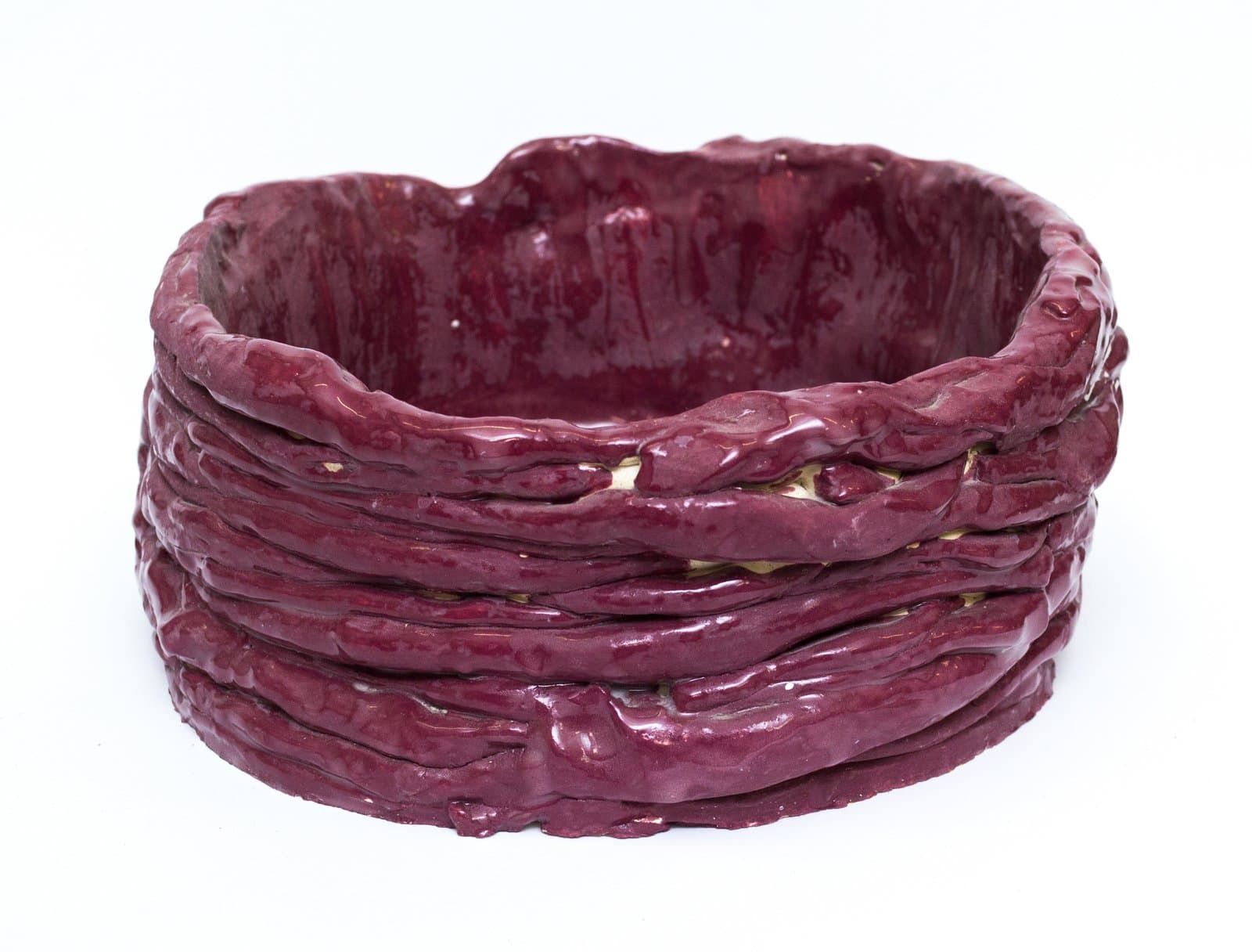 Ceramic bowl with coil-built walls in deep burgundy glaze, roughly oval form with textured rope-like exterior bands.