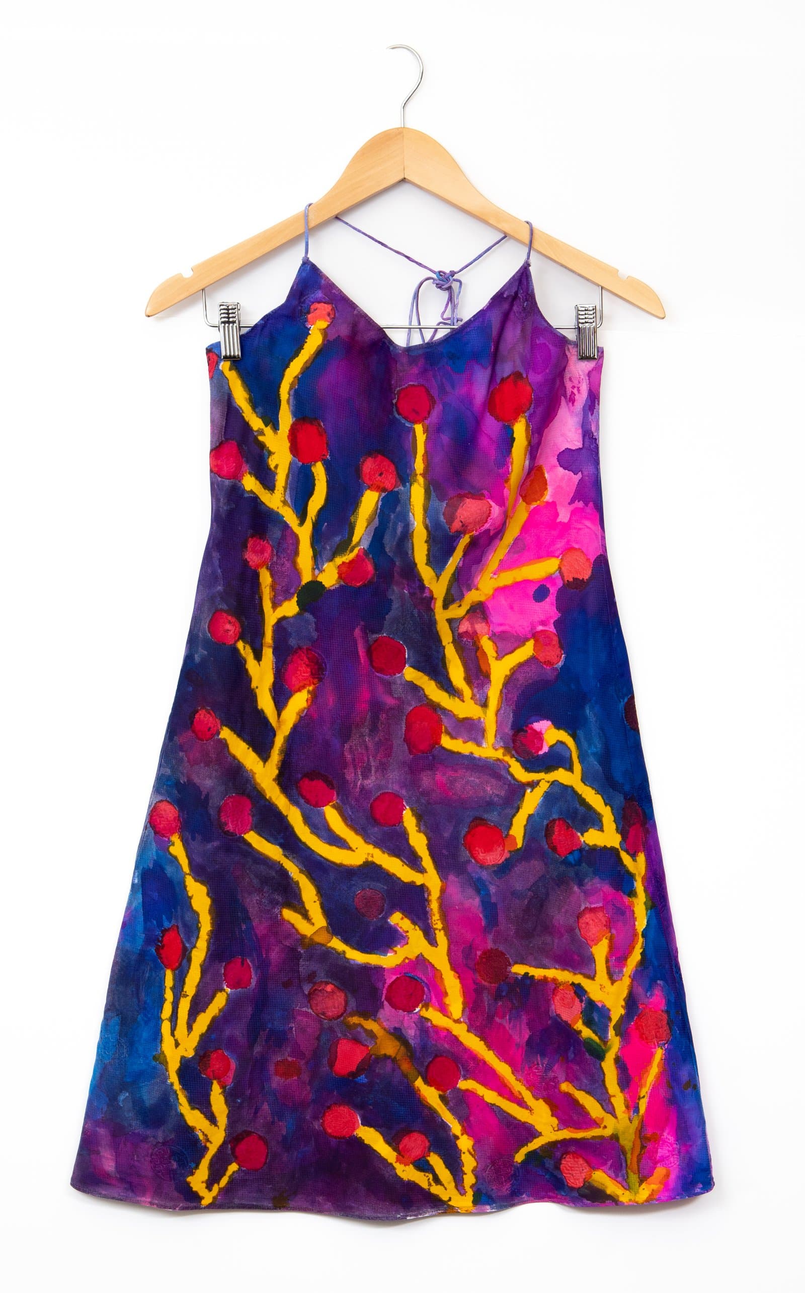 Hand-painted slip dress on a wooden hanger, featuring bold yellow branching forms with red circular dots on a purple and pink background.