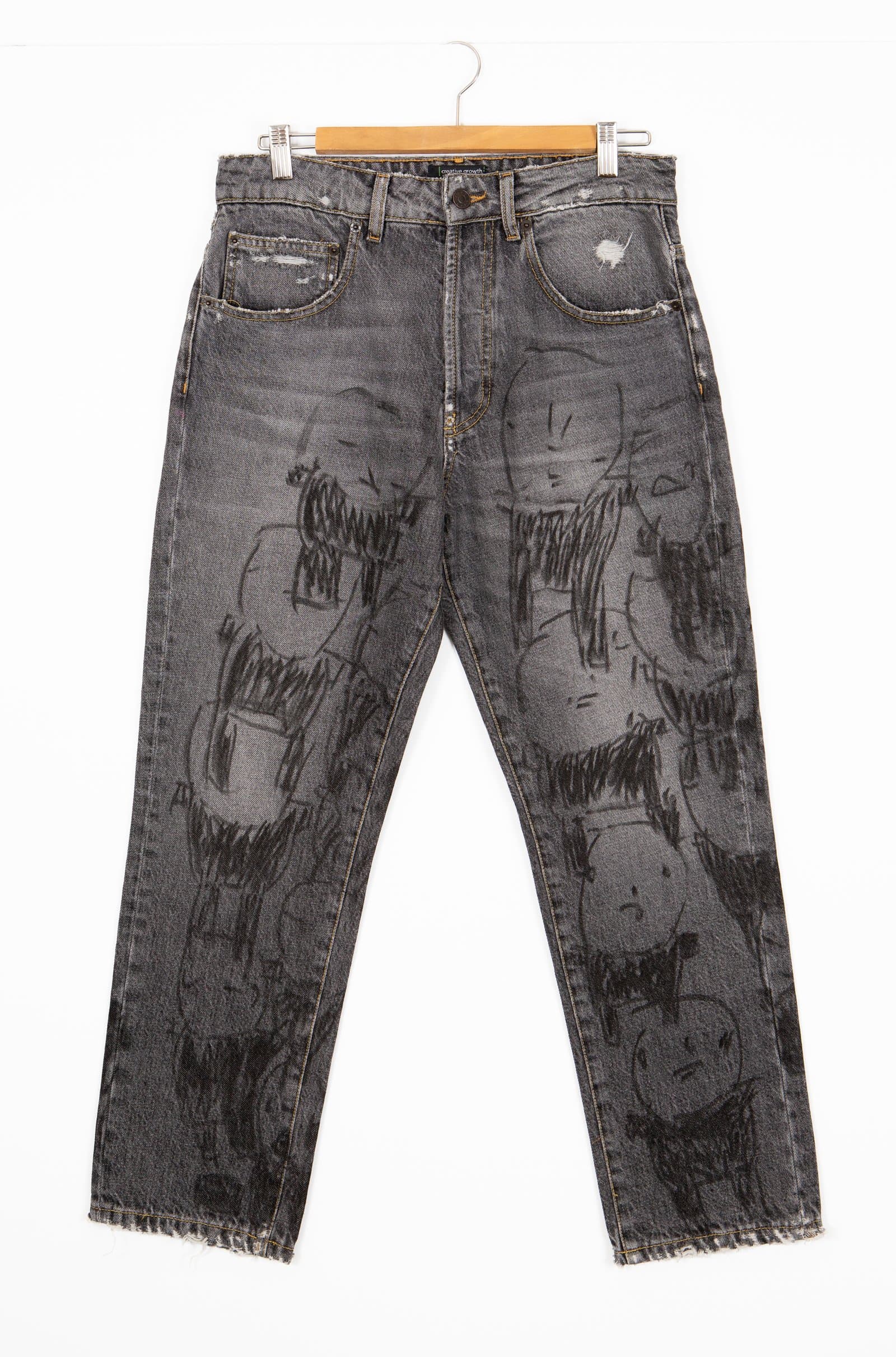Gray denim jeans covered in black marker drawings of expressive cartoon-like figures with open mouths and wild hair.