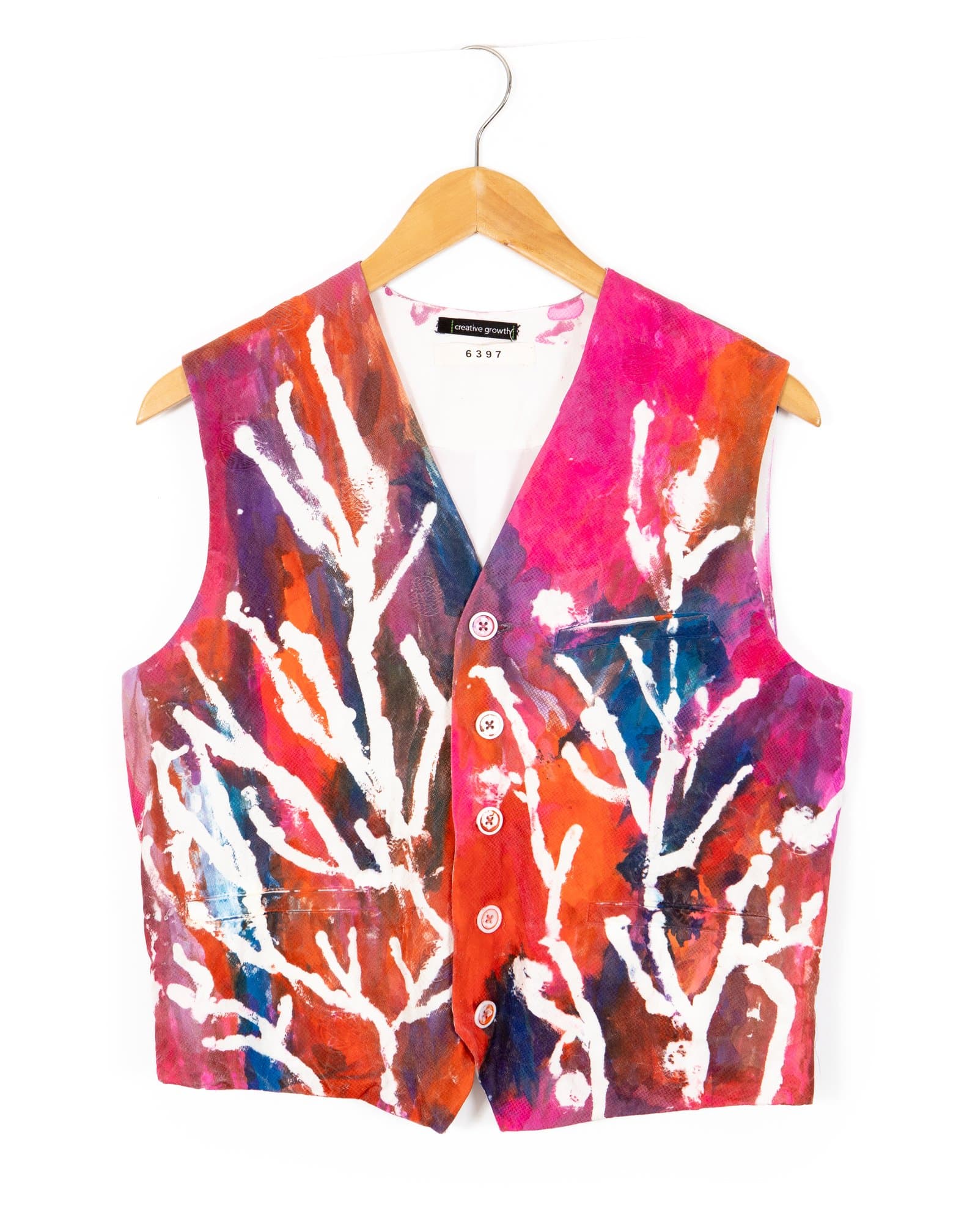Hand-painted fabric vest on a wooden hanger with white branching forms on a vivid red, pink, purple, and blue background.