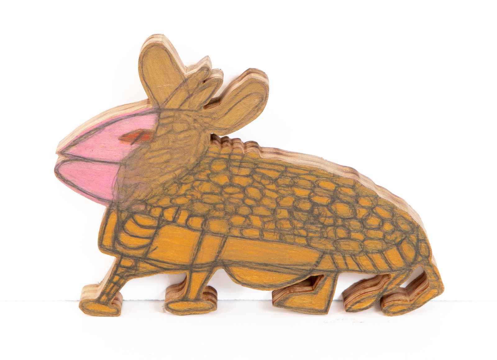 Armadillo-like creature drawn in Prismacolor on a wood cutout, rendered in golden yellow with pink and red accents.
