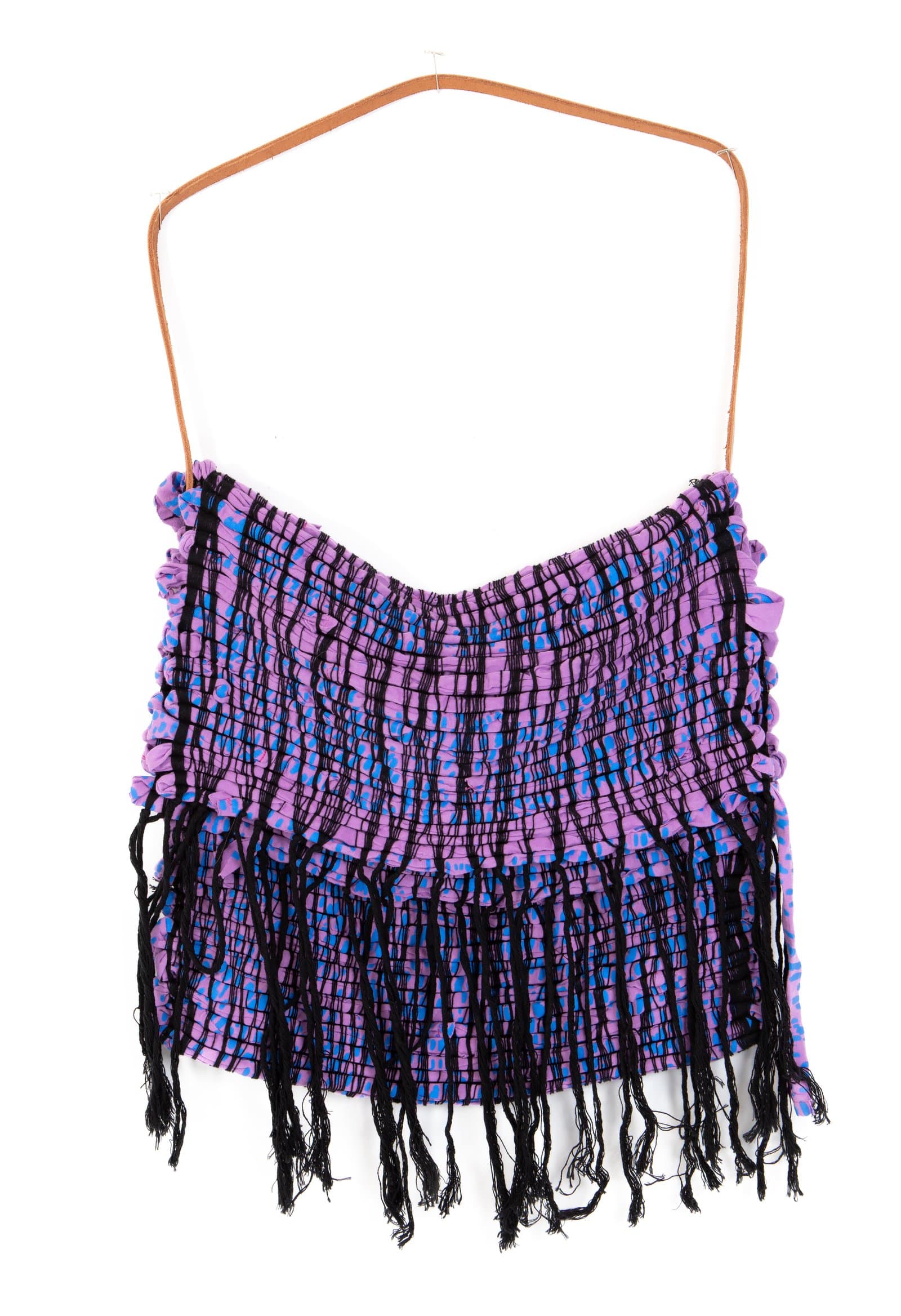 Woven textile bag in purple and blue patterned fabric with black yarn fringe, hung on a wooden hanger against white background.