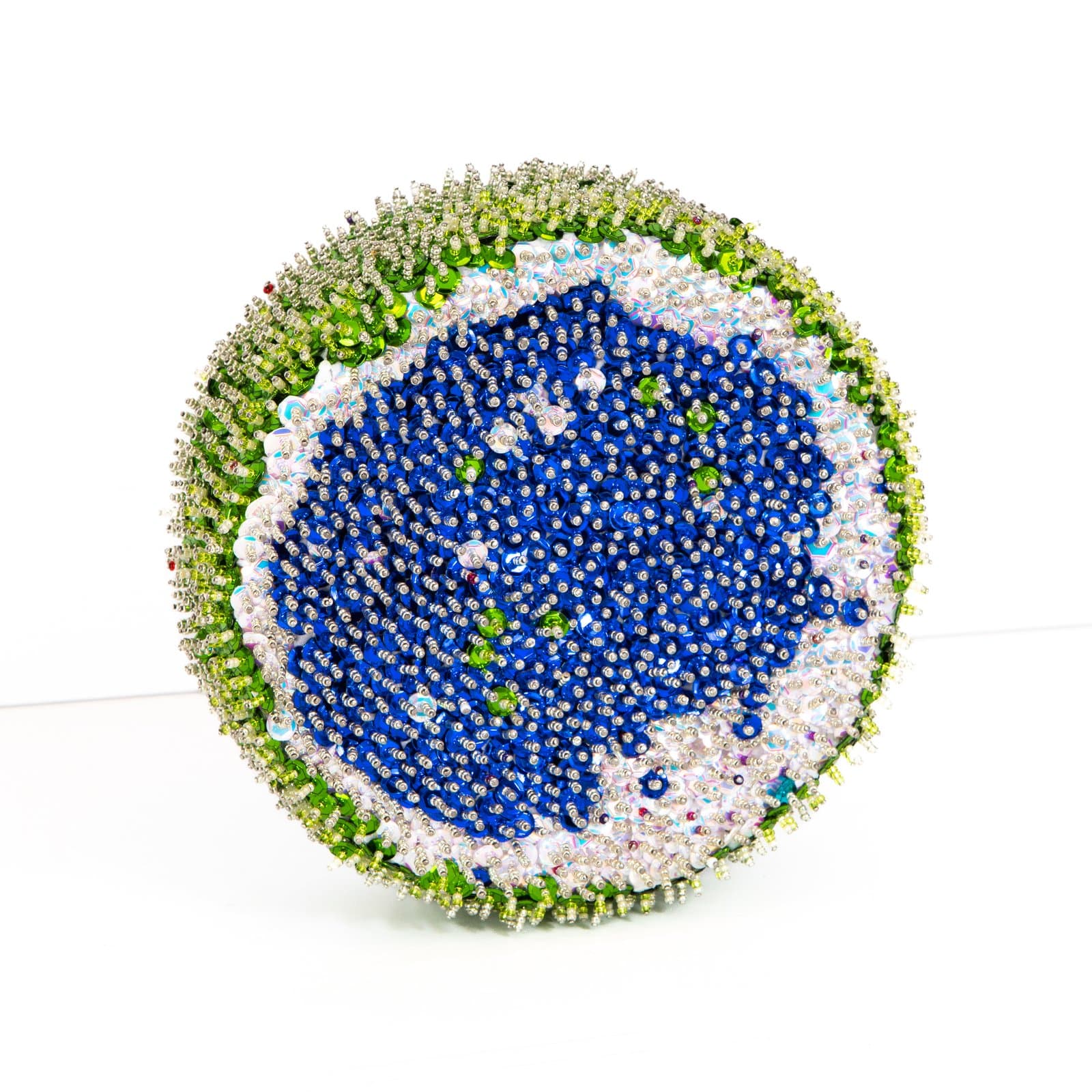 Spherical sculpture densely covered in blue, silver, white, and green sequins arranged in concentric circular patterns.
