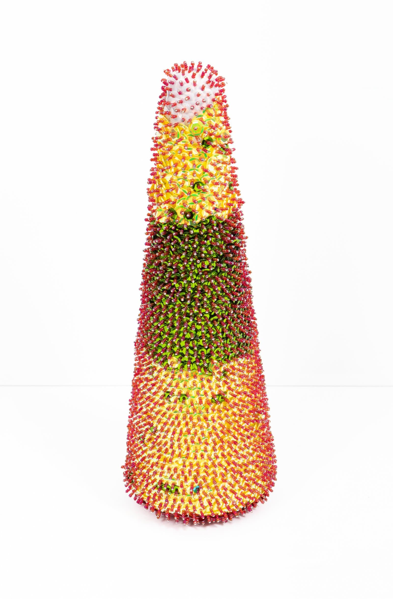 Tall cone-shaped sculpture densely covered in red, yellow, and green sequins on a white background.
