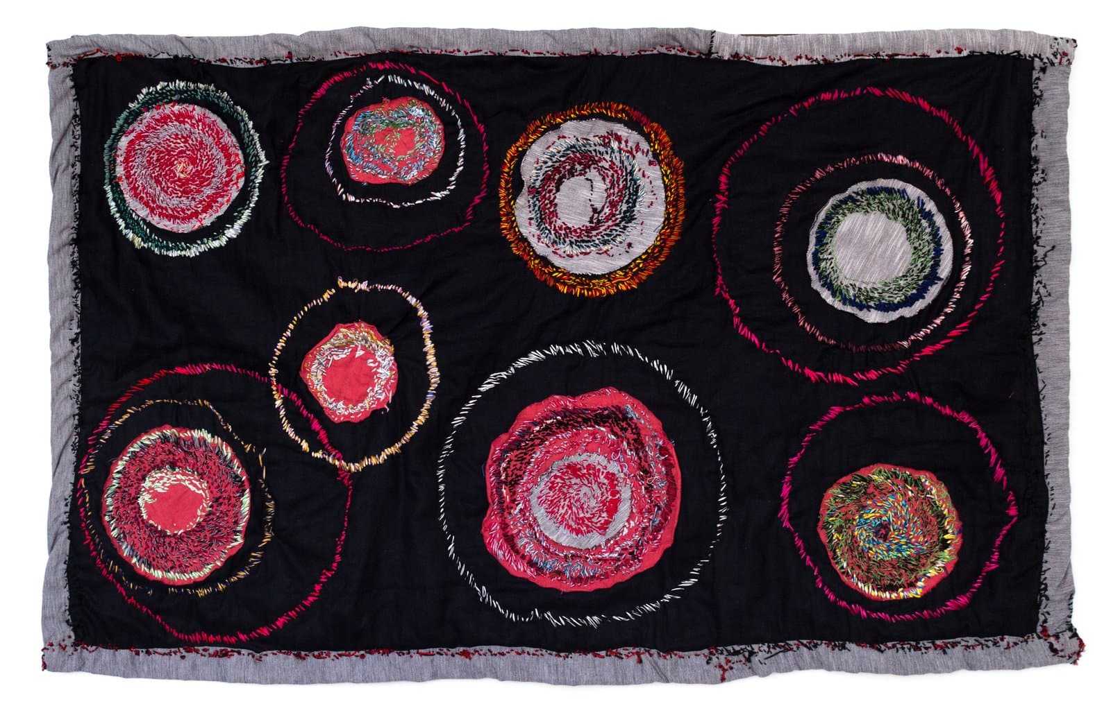 Embroidered textile with nine multicolored circular forms on black fabric, with frayed gray border edges.