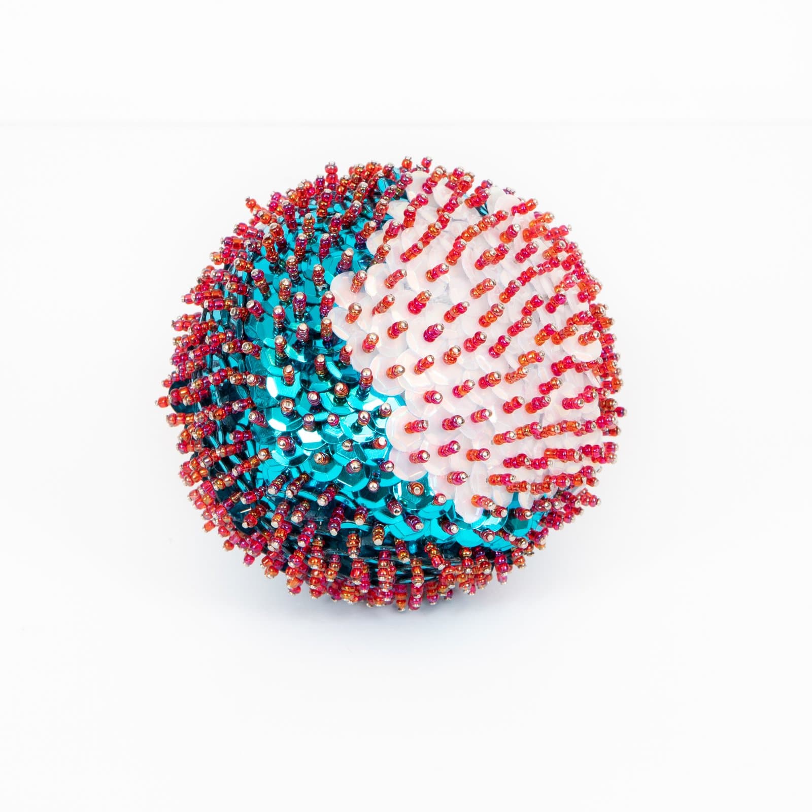 Spherical sculpture densely covered in red-orange beaded pins and teal sequins arranged in swirling sections on white styrofoam.