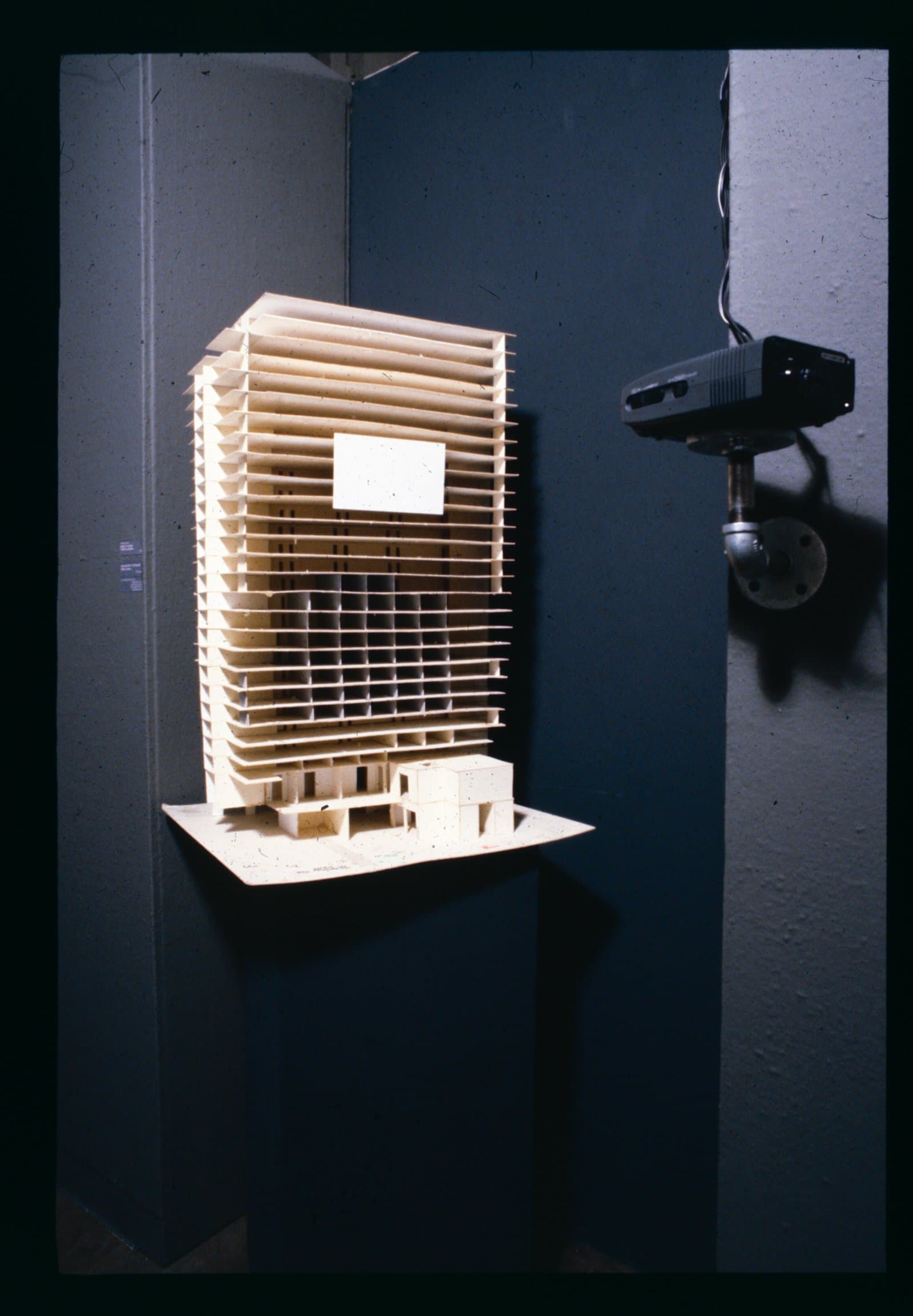 Architectural scale model of a multi-story building constructed from cream-colored cardboard or foam board, displayed on a shelf.