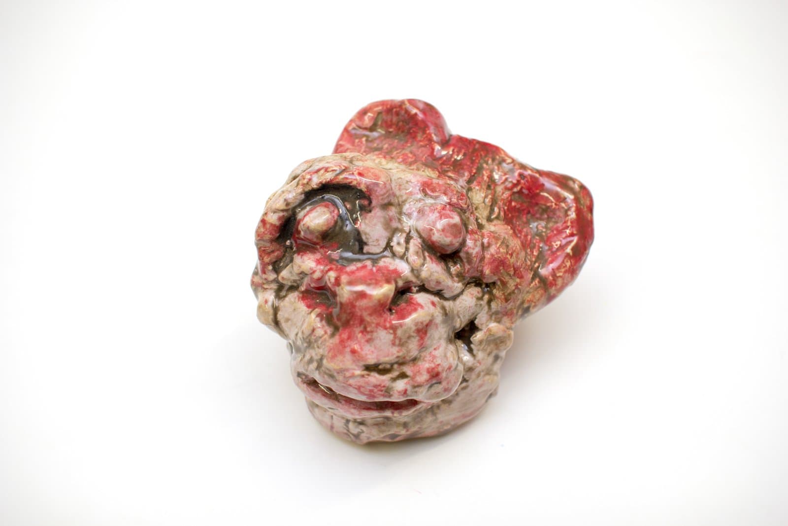 Small ceramic sculpture of a face with textured surface, glazed in red, cream, and dark brown tones.