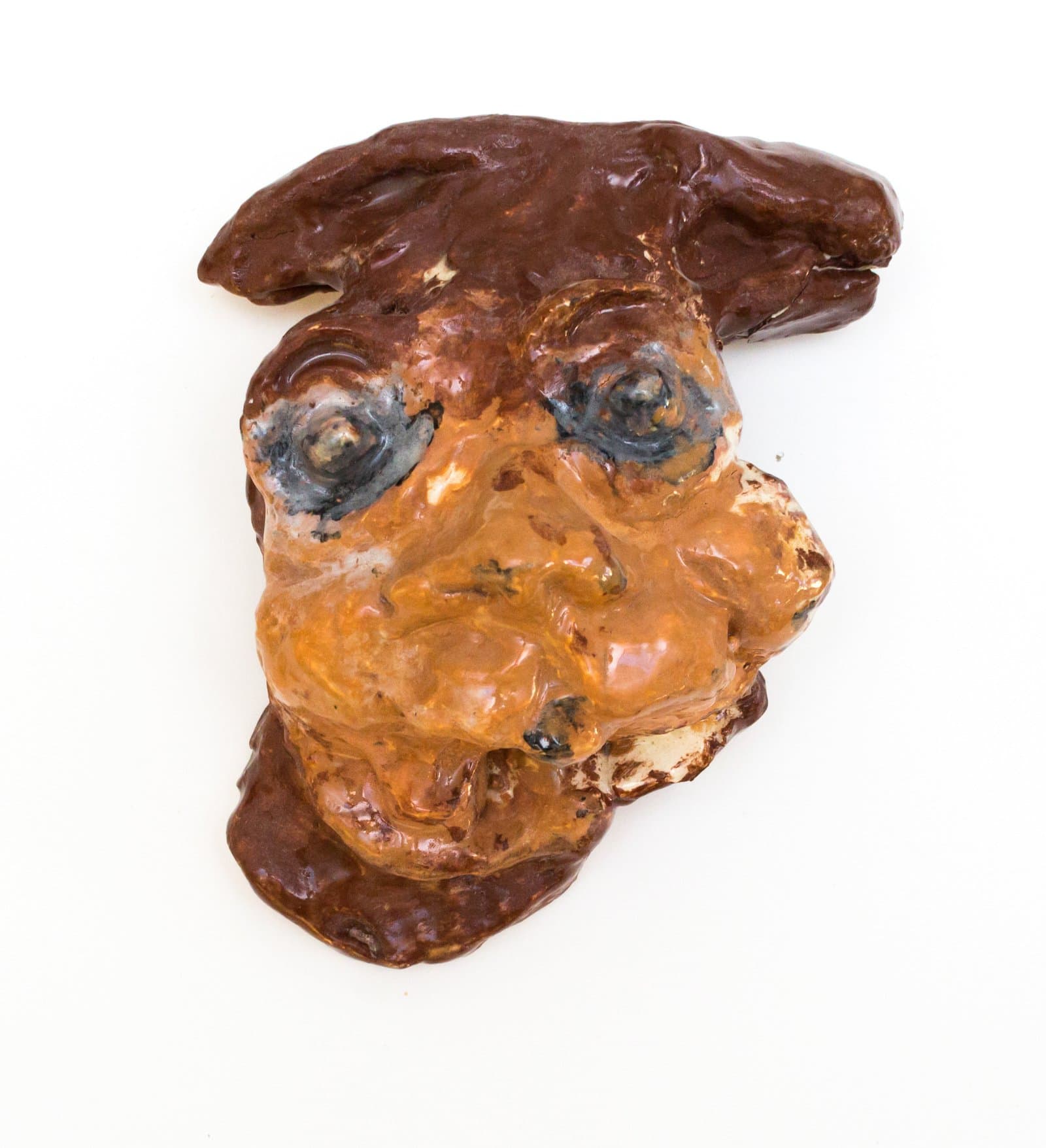 Glazed ceramic wall sculpture depicting a stylized face with dark brown hair, orange-brown skin tones, and blue-gray eyes.