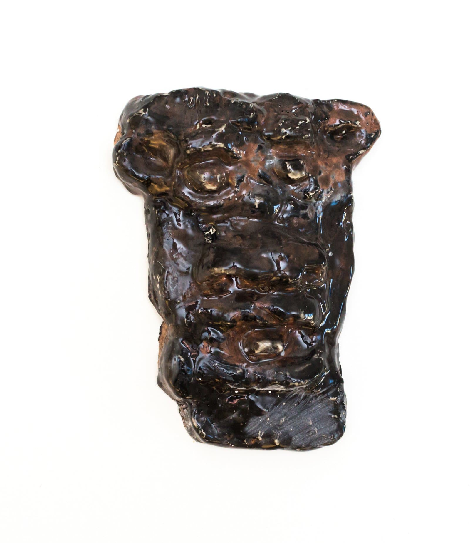 Small glazed ceramic face mask with roughly modeled features, covered in a deep dark brown glossy glaze, on white background.