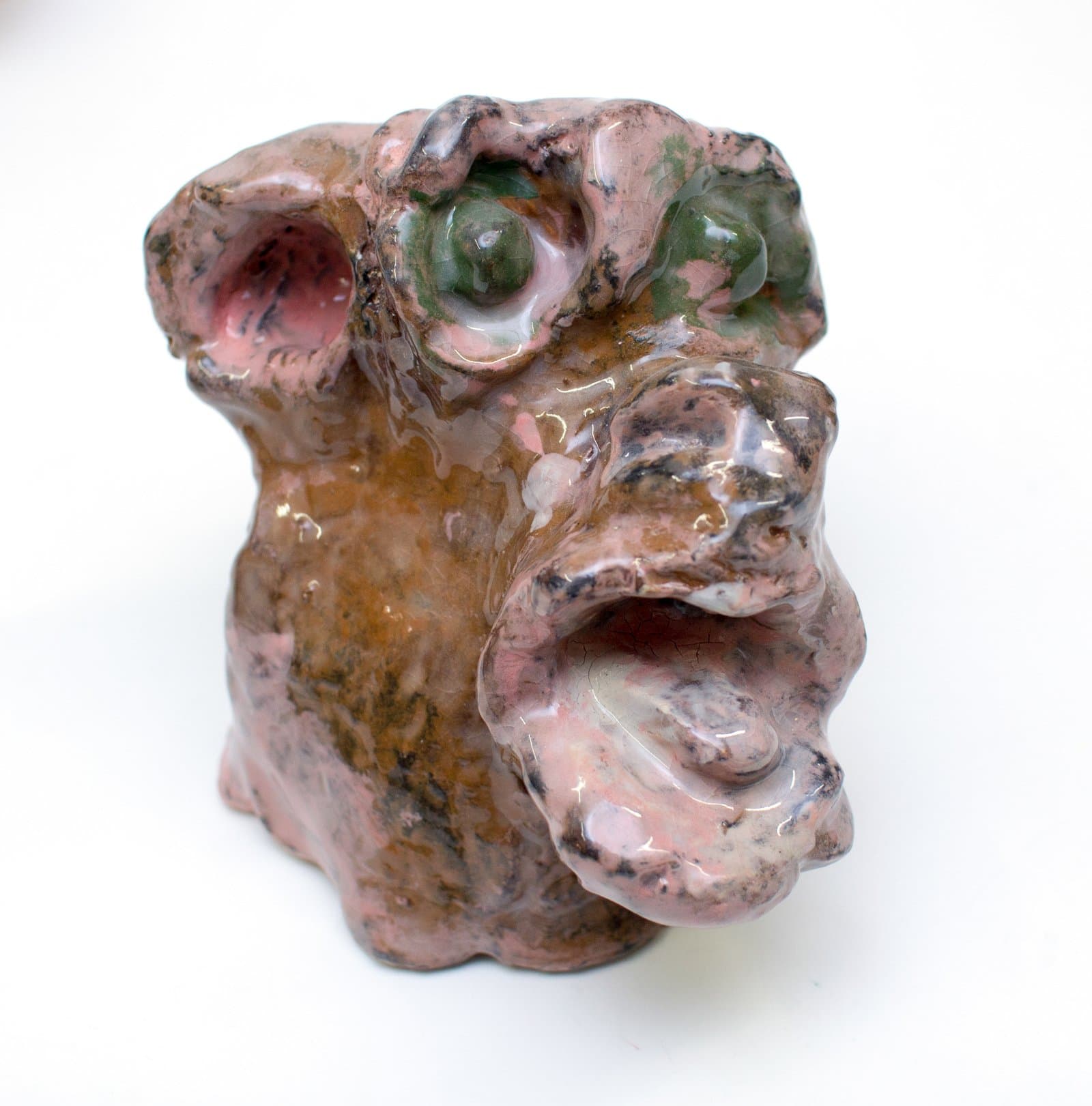 Glazed ceramic sculpture of a face with bulging green eyes and open mouth in pink, brown, and black tones.
