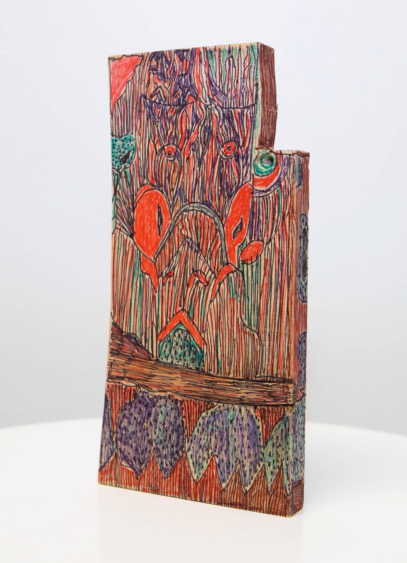 Mixed media sculpture on wood with colorful pen drawings of abstract faces, flora, and geometric patterns
