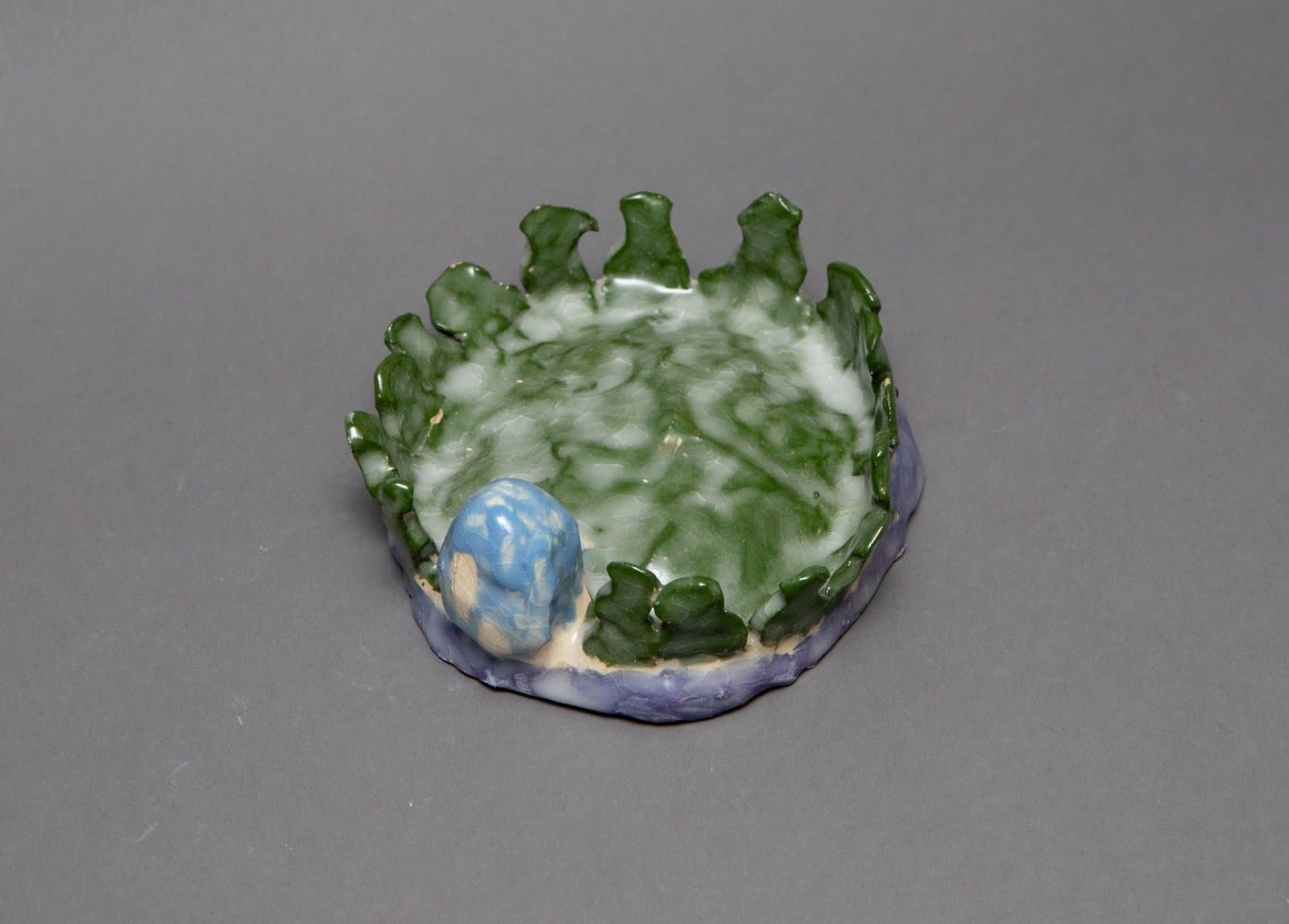 Ceramic bowl with irregular rim featuring green, white, blue, and purple glazes with sculptural elements.