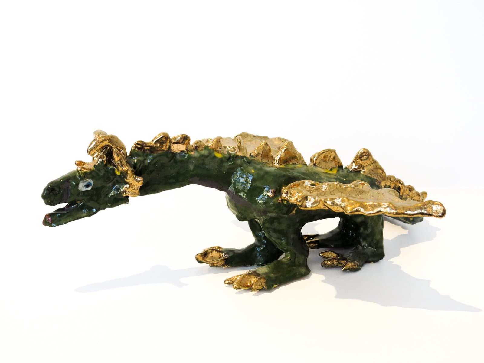 Ceramic sculpture of a dragon-like reptile in dark green glaze with metallic gold accents on spines, claws, and back plates.