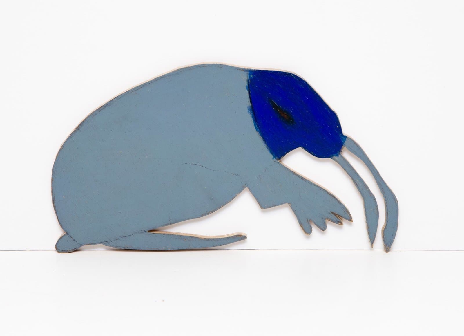 Cut-out painted wood sculpture of an elephant in profile with gray body, blue head area, and white tusks on white background.