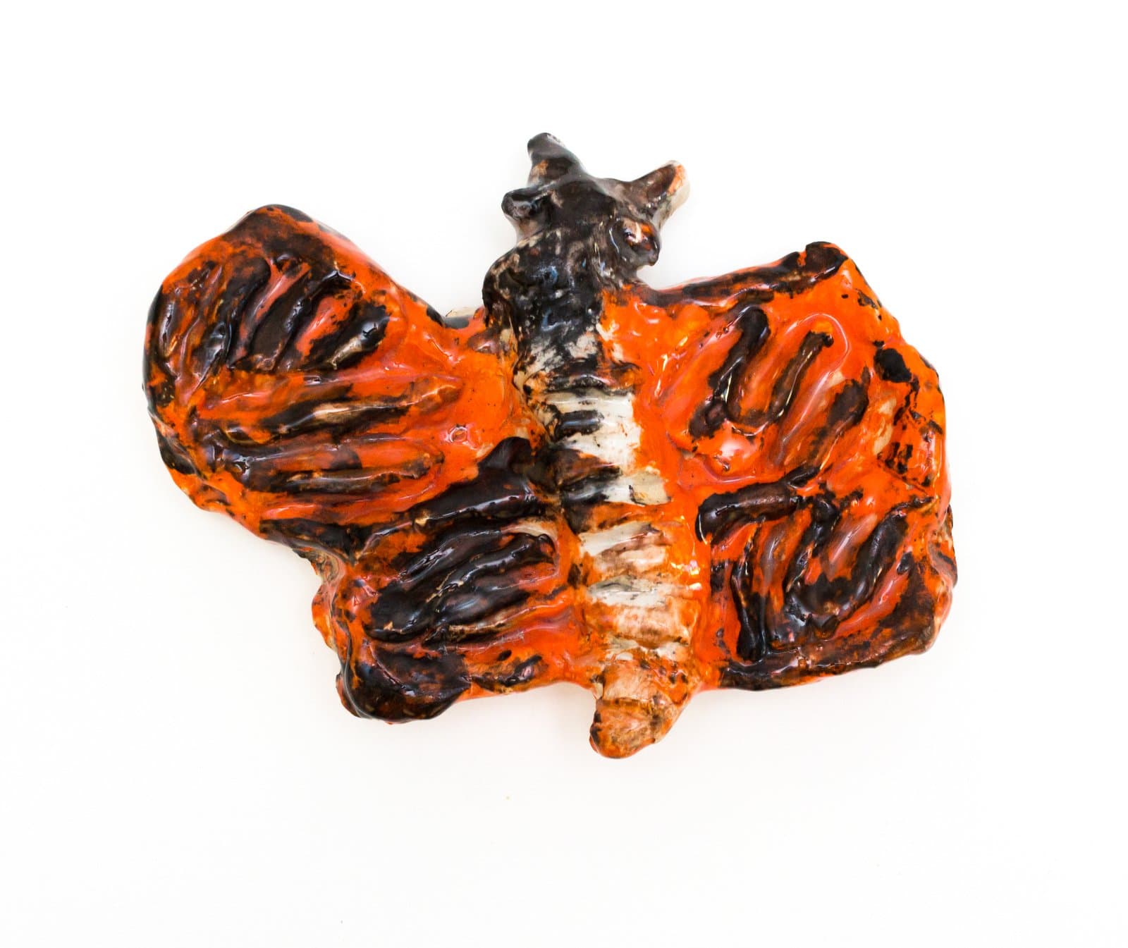 Glazed ceramic sculpture of a reclining animal figure with bold orange and black striped patterning on white background.