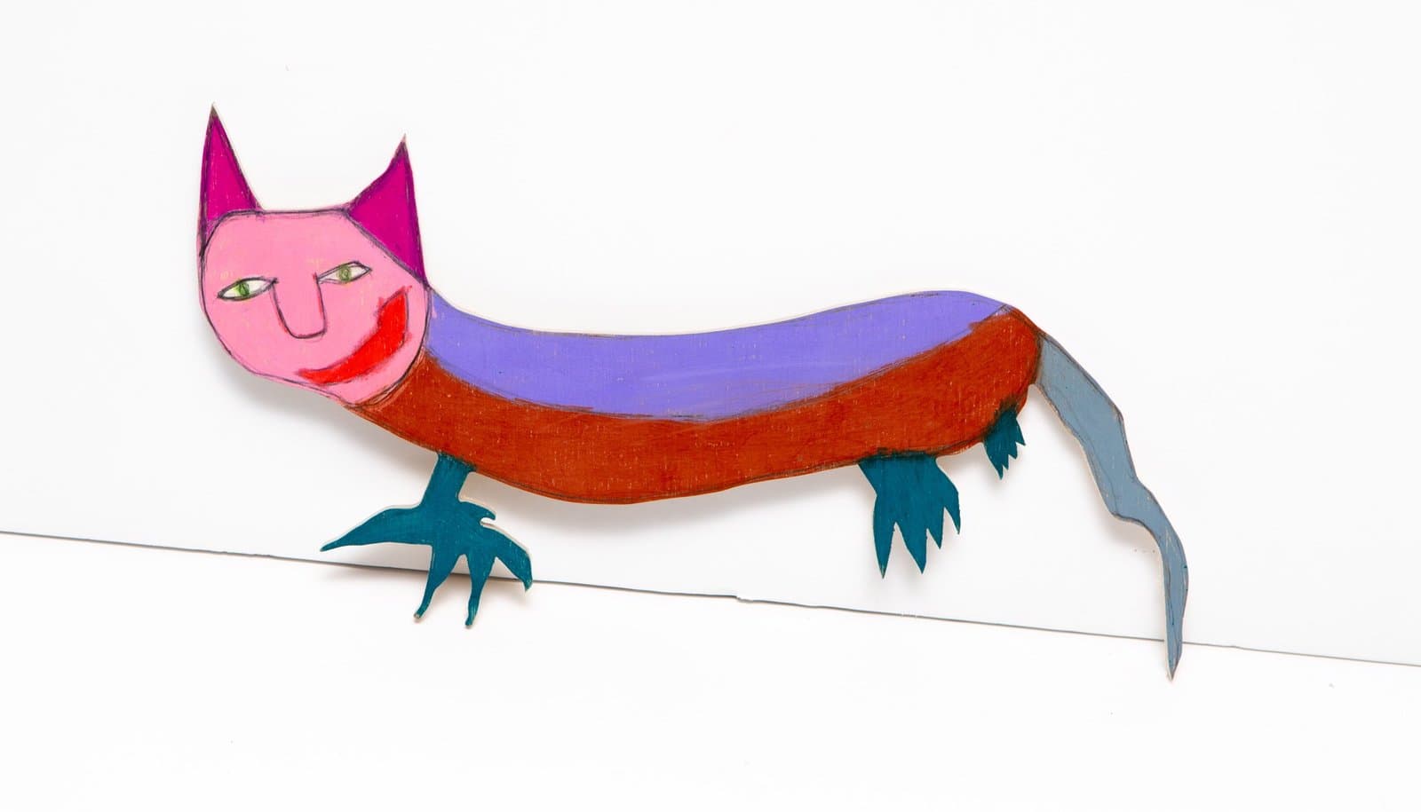 Painted wood sculpture of an elongated cat-like creature with pink face, purple ears, and colorful striped body.