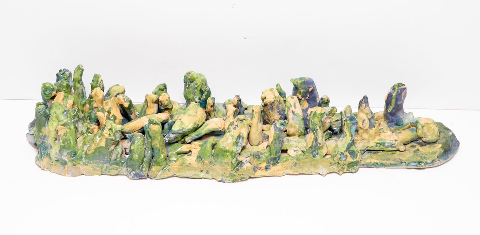 Ceramic sculpture with numerous small figurative forms in green and yellow glazes arranged on an elongated base.