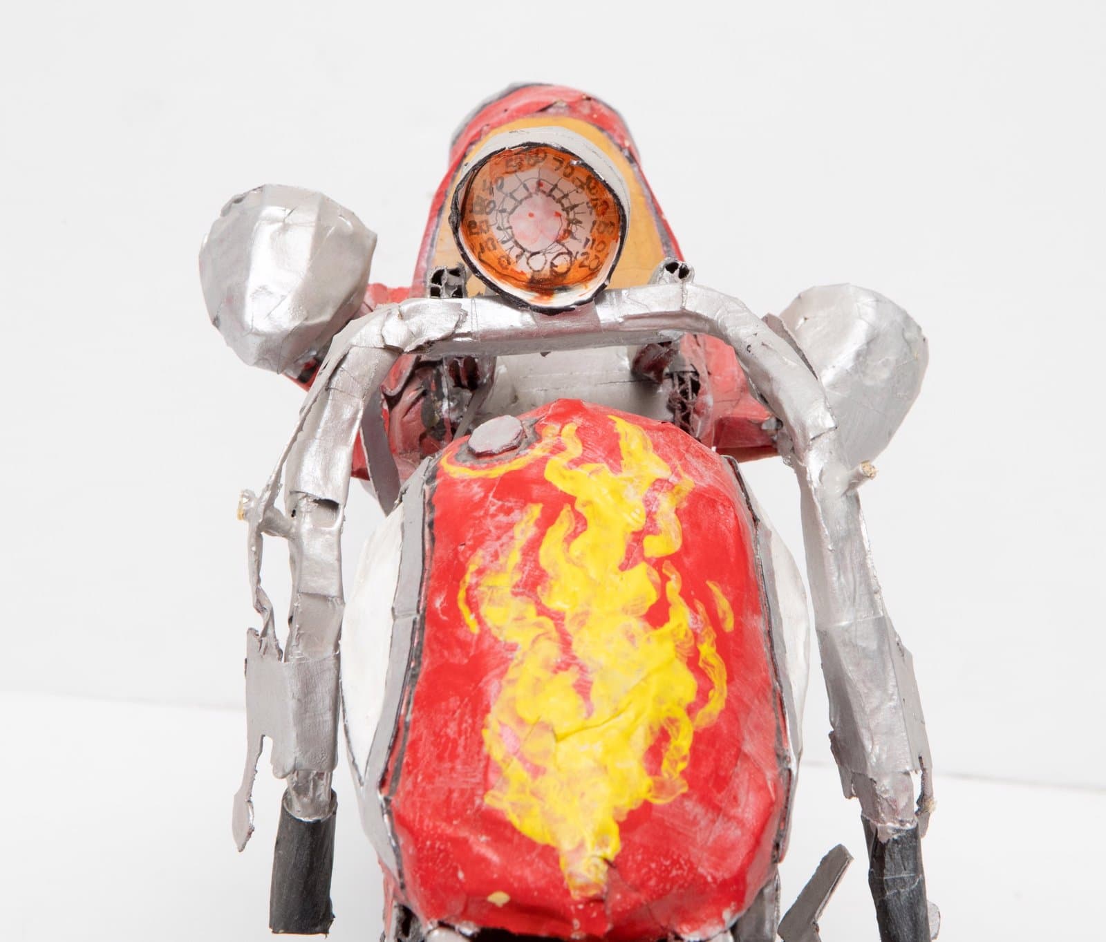 Cardboard sculpture of humanoid figure with silver body, red and yellow torso, and circular head element with orange interior.