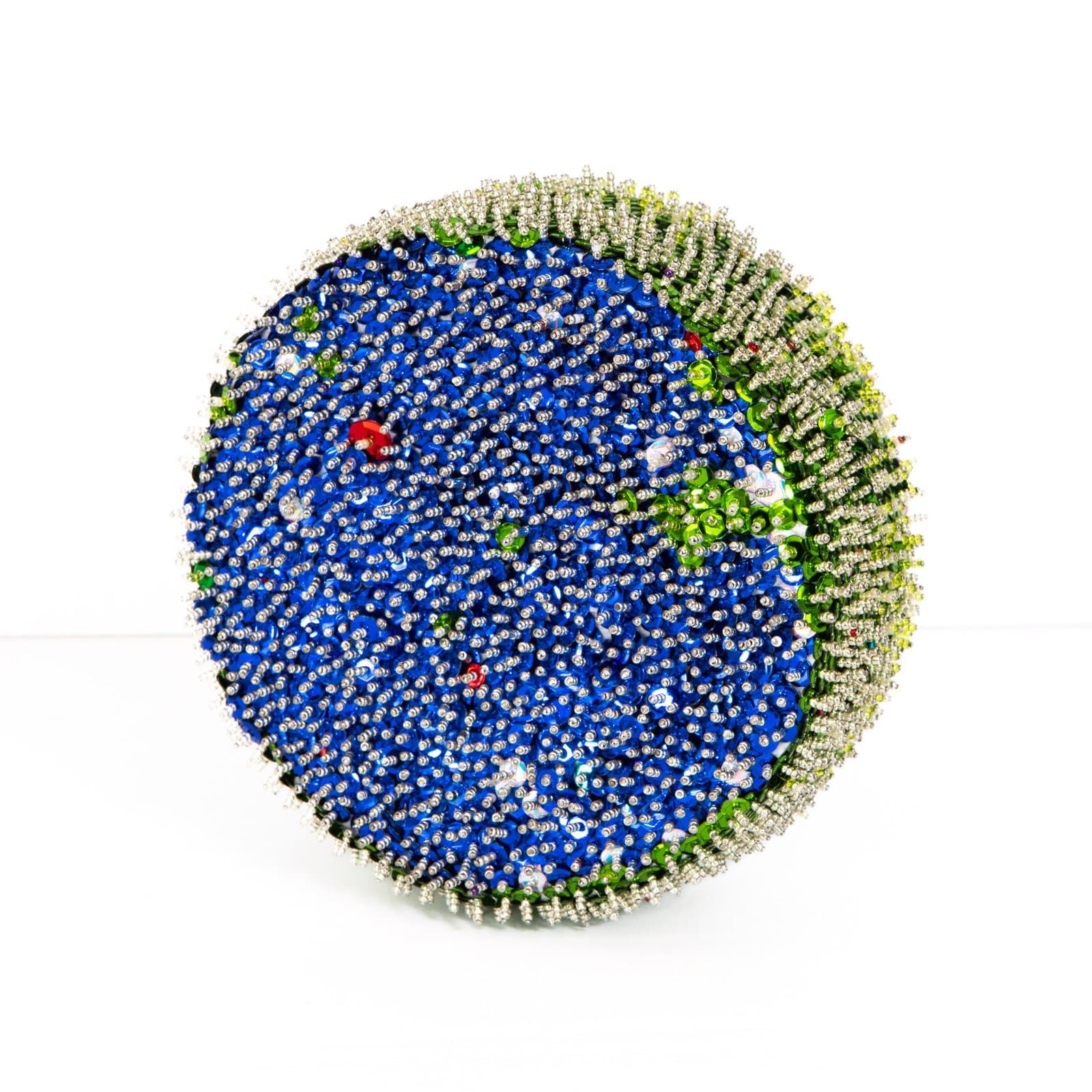 Circular sculpture covered in sequins, predominantly blue center with green and silver border, mounted on styrofoam.