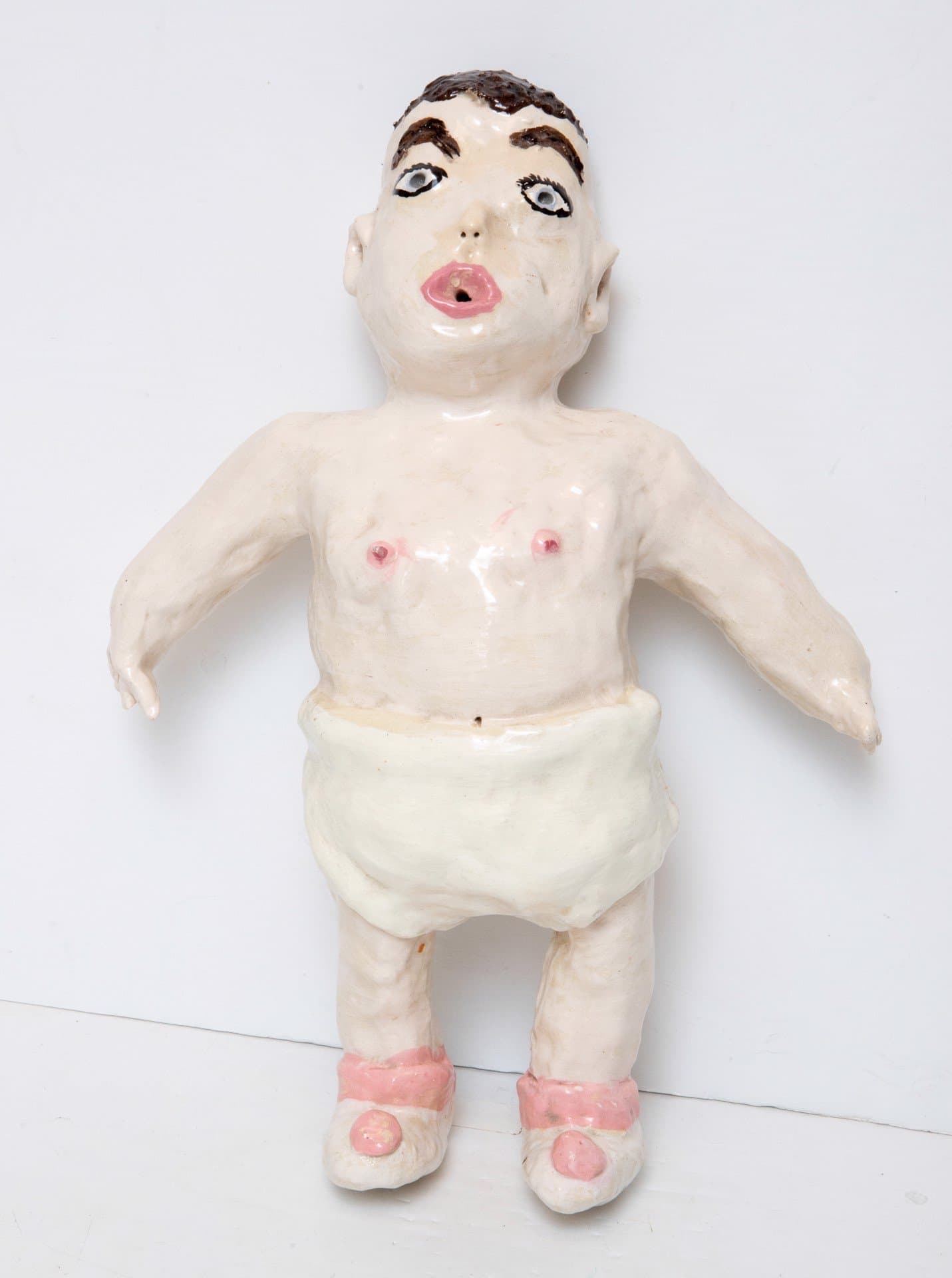 Ceramic figurative sculpture of a nude human form with brown hair, pink lips, and pink shoes on white background.