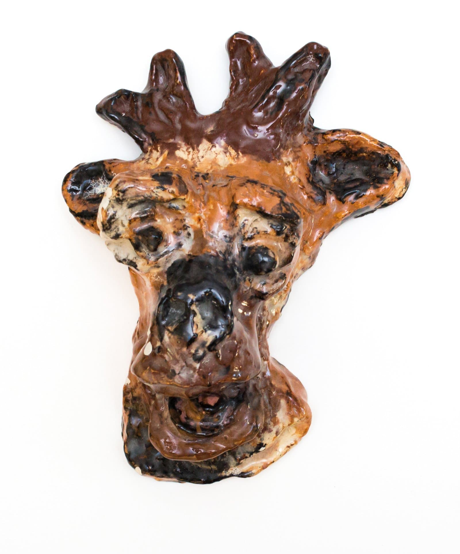 Glazed ceramic wall sculpture of an animal face with antler-like projections, in brown, black, and cream tones.