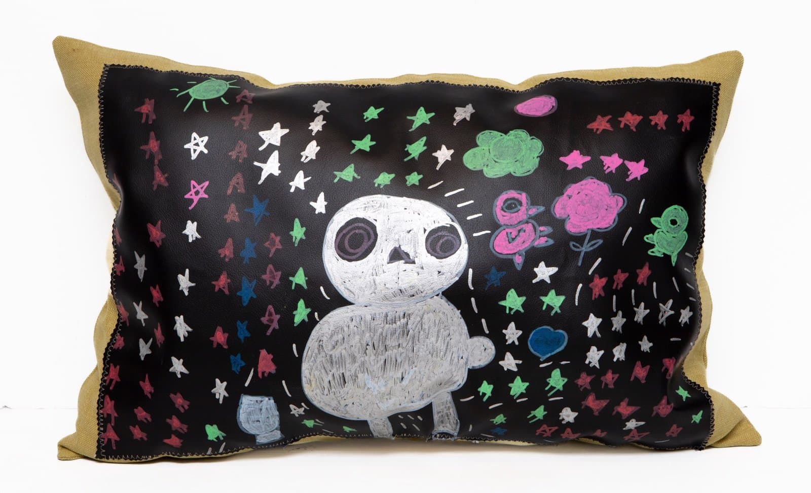 Decorative pillow with black leather center panel featuring white skull figure surrounded by colorful stars on tan fabric.
