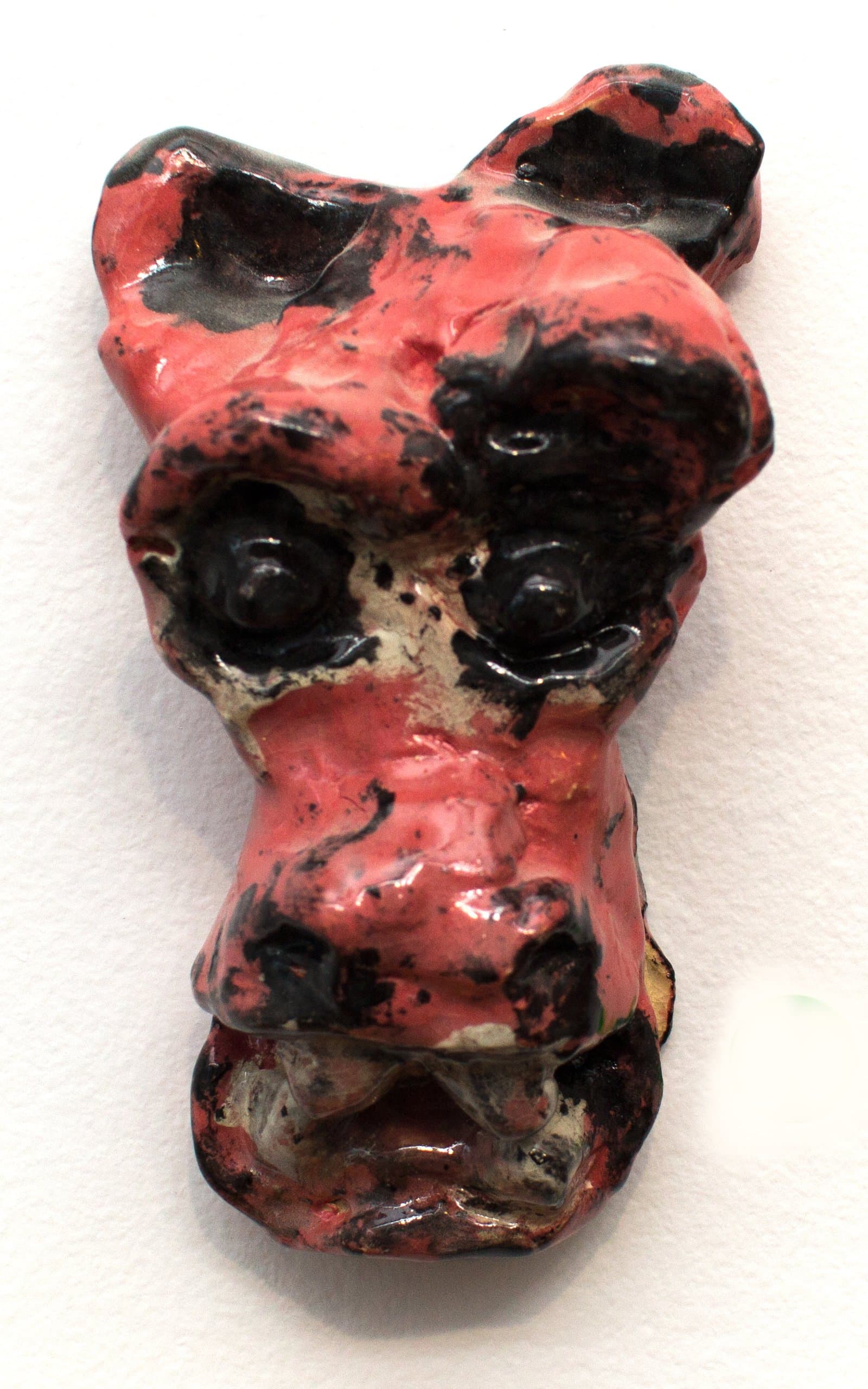 Small glazed ceramic wall sculpture depicting a stylized animal face in red and black glaze with protruding eyes.