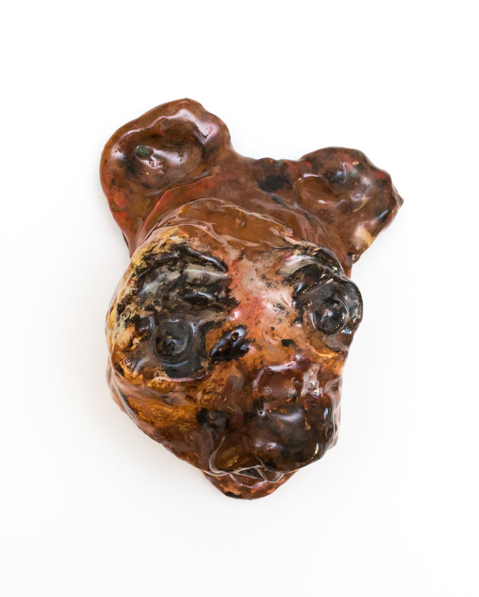 Small glazed ceramic sculpture with an irregular, lumpy form suggesting a face, in deep reddish-brown and black tones.