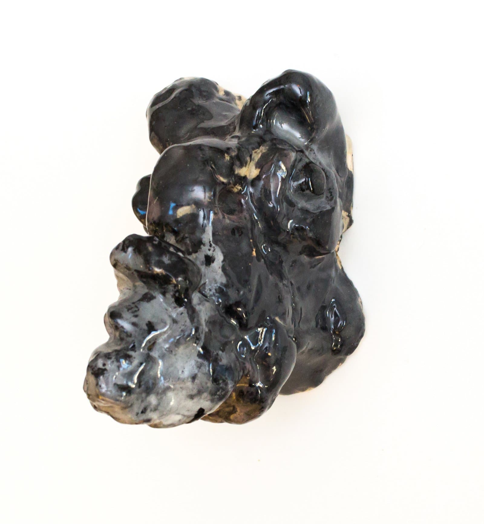 Abstract ceramic wall sculpture with lumpy, organic forms covered in a glossy black glaze, photographed against white background.