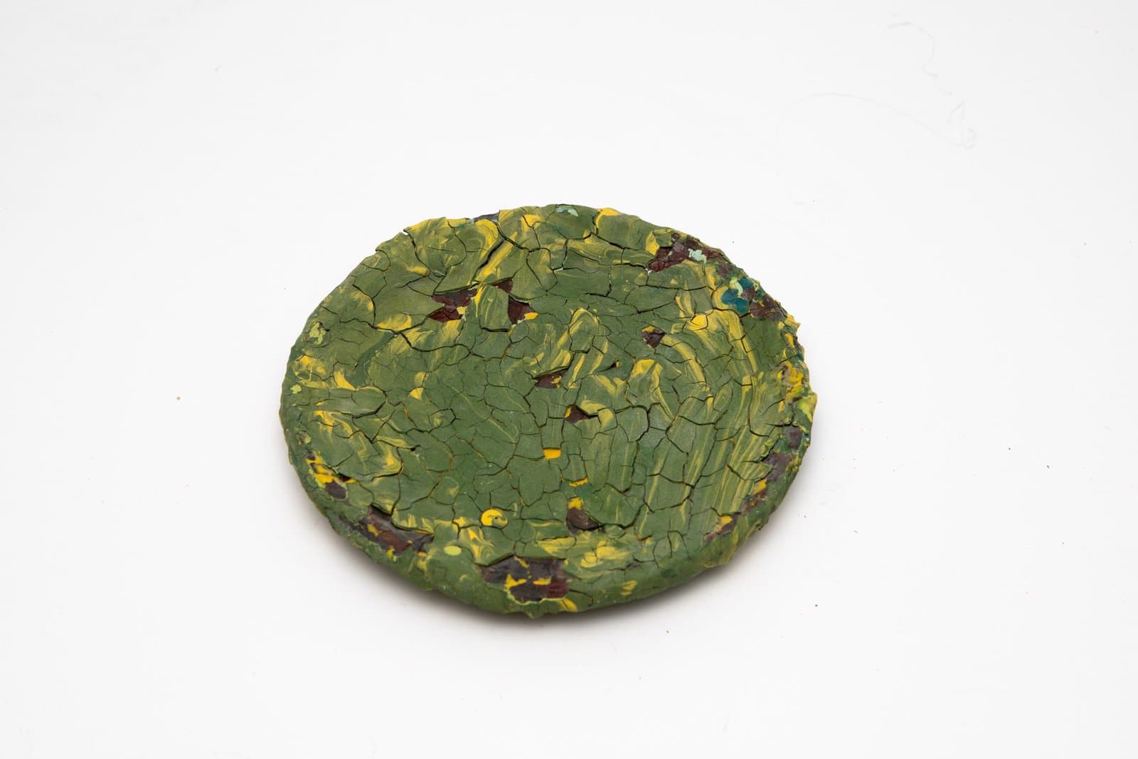 Circular ceramic plate with crackled green glaze and yellow and burgundy accents on white background.