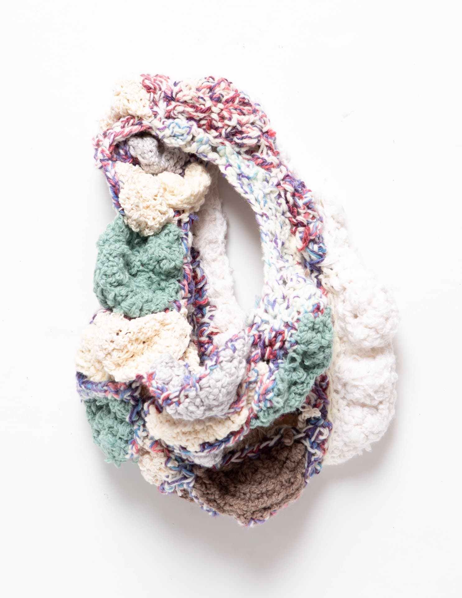 Crocheted textile sculpture with interwoven chains in multicolored yarn including mint green, cream, and brown sections.