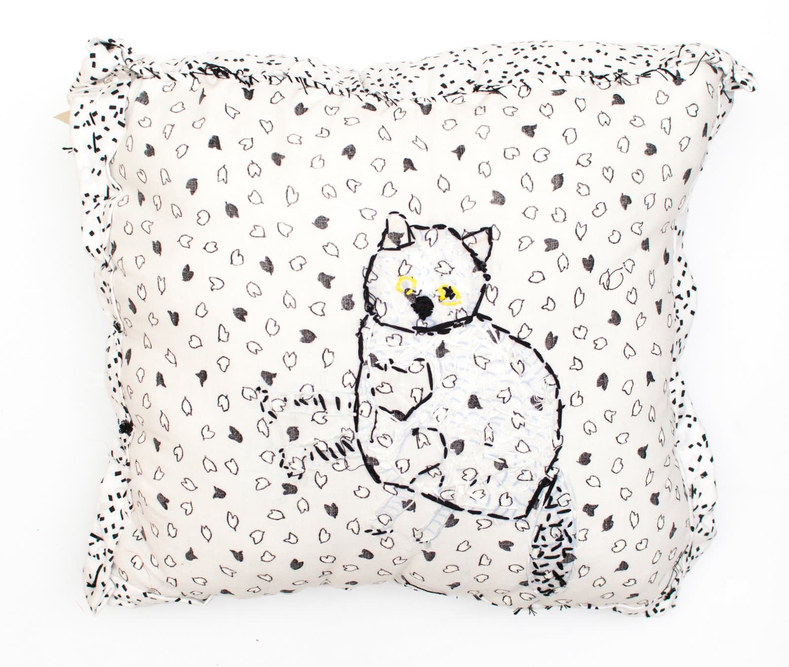 Embroidered fabric pillow depicting a seated cat in black thread on cream fabric scattered with small heart motifs.