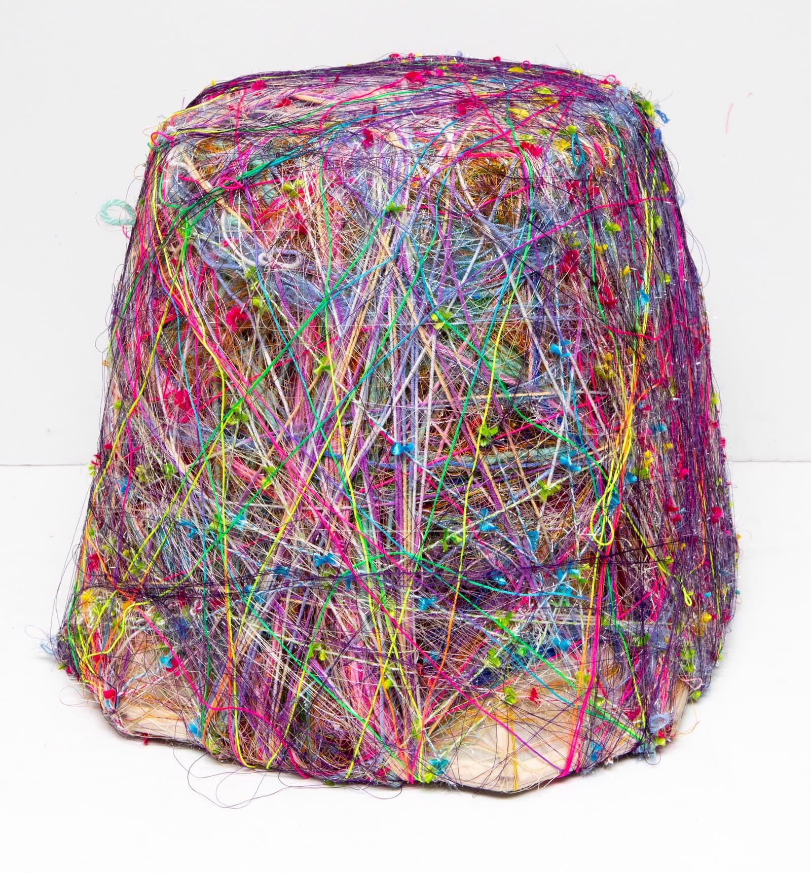 Cube-shaped sculpture densely wrapped in multicolored yarn and thread creating an abstract fiber artwork.