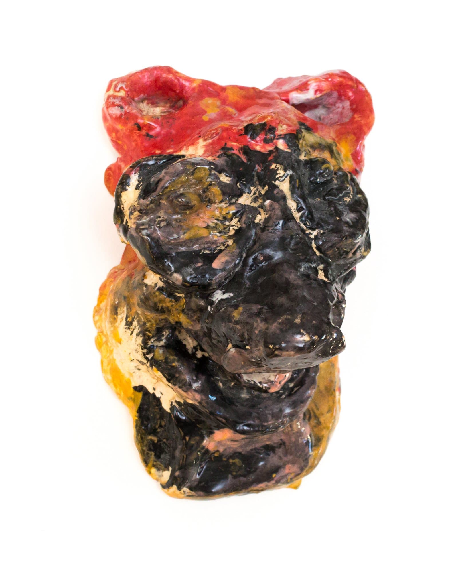 Small abstract ceramic sculpture with lumpy organic form, glazed in black, red, orange, and cream on white background.