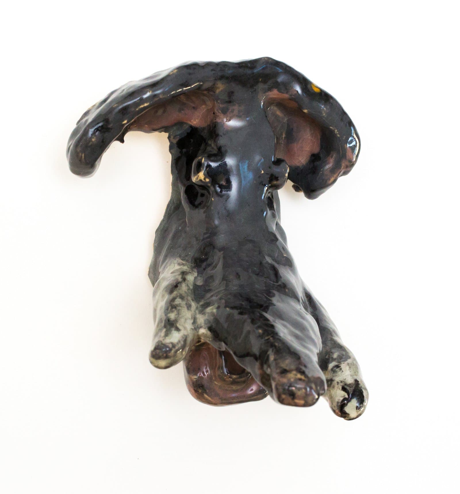 Small glazed ceramic sculpture of a dog viewed from above, predominantly dark black and brown with mottled gray paws.