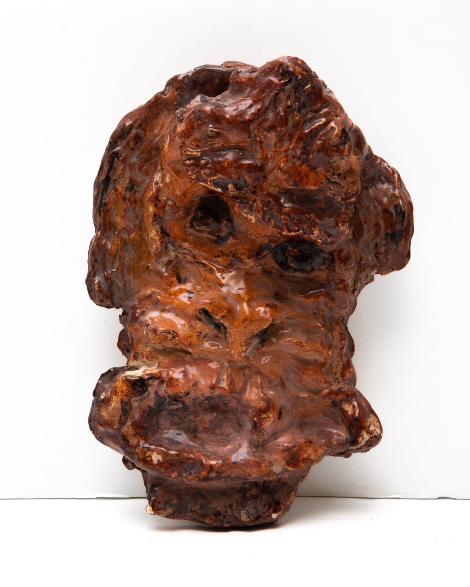 Ceramic sculpture of distorted head with hollow eye sockets in brown glazed earthenware