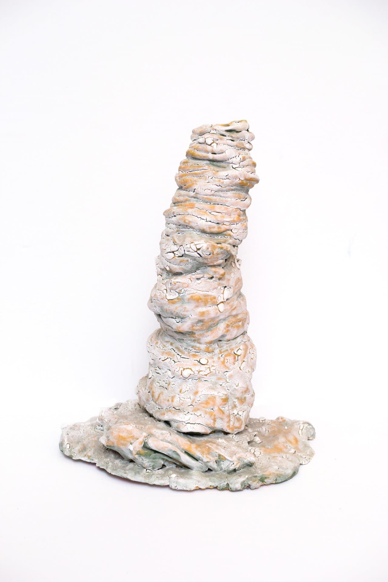 Ceramic sculpture with stacked cylindrical forms in muted tones on irregular base against white background