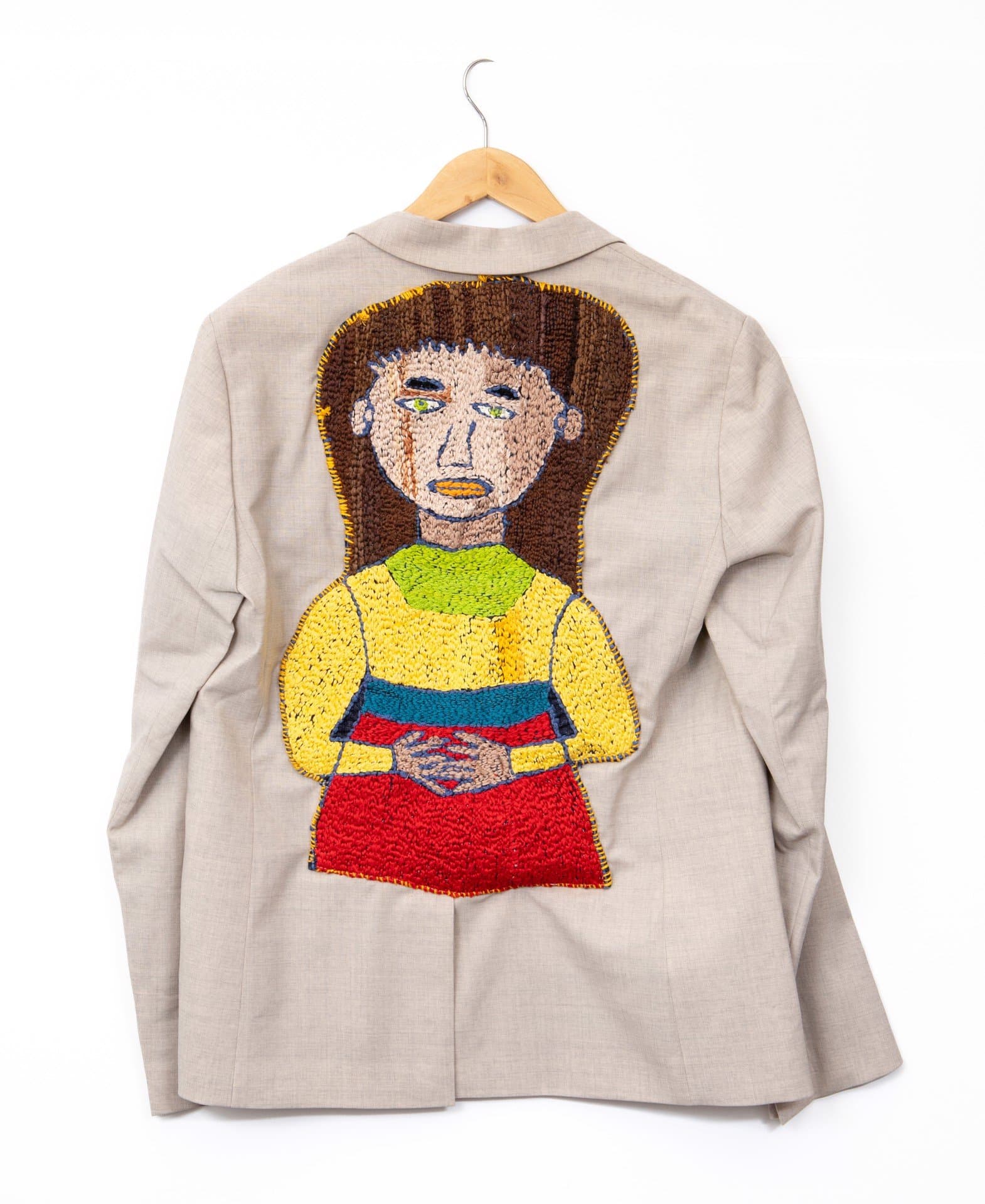 Embroidered portrait of a figure on the back of a beige blazer, featuring colorful thread work in yellow, red, and blue.
