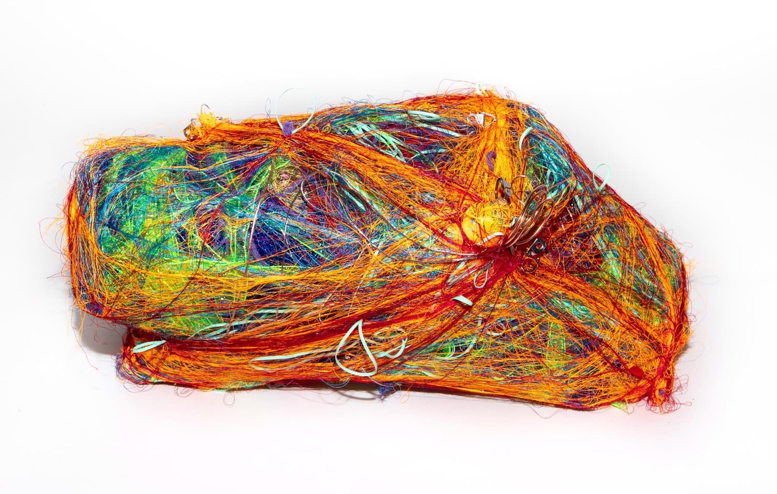 Sculptural form made of densely wrapped multicolored threads in orange, green, blue, and red on white background.