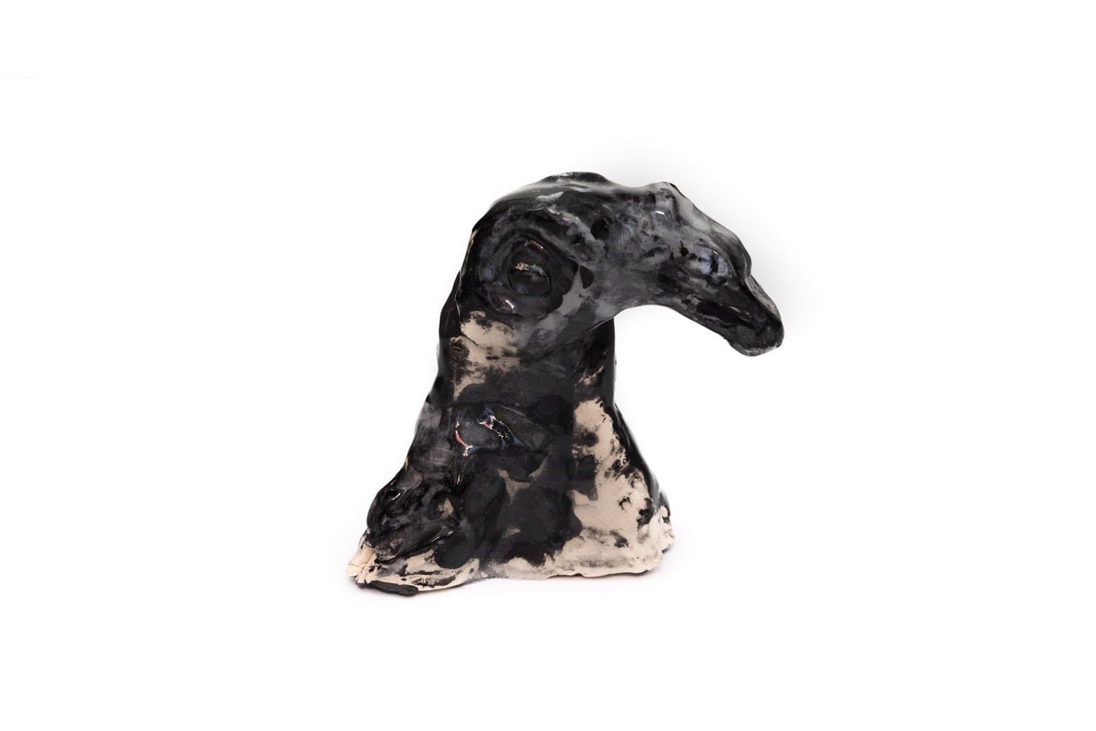 Ceramic sculpture of a dog's head and neck in black glaze with tan patches on white background.