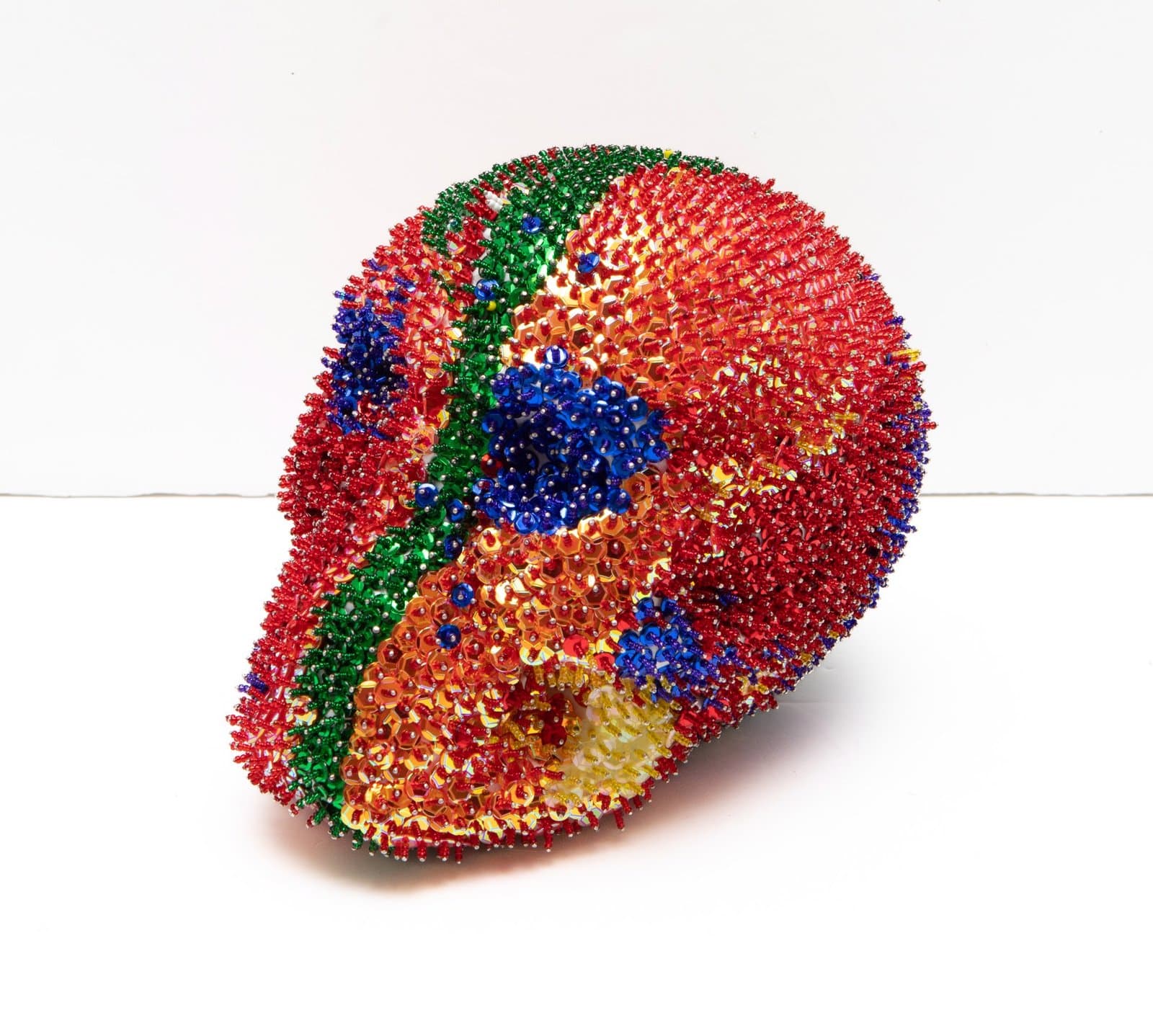 Circular sculptural form densely covered in multicolored sequins in red, blue, green, and gold creating a textured surface.