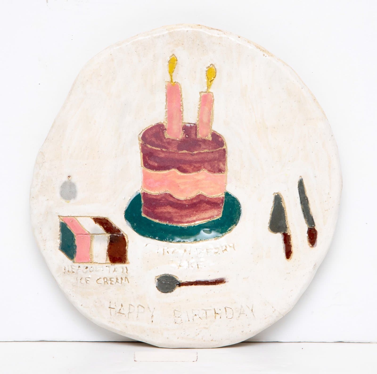 Circular ceramic plate painted with birthday cake, ice cream, utensils, and 'HAPPY BIRTHDAY' text in mixed colors