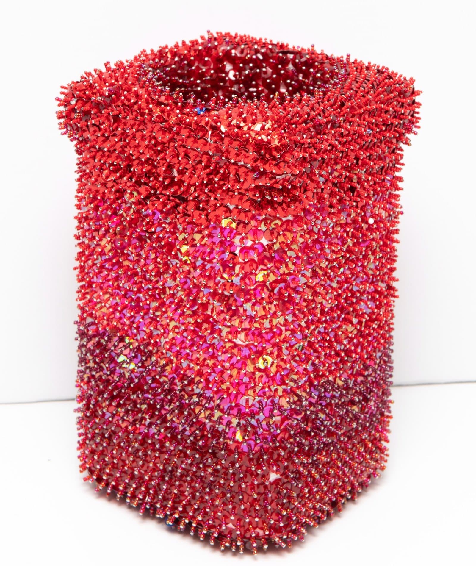 Cylindrical vessel sculpture covered entirely in red and pink sequins creating a textured, shimmering surface.