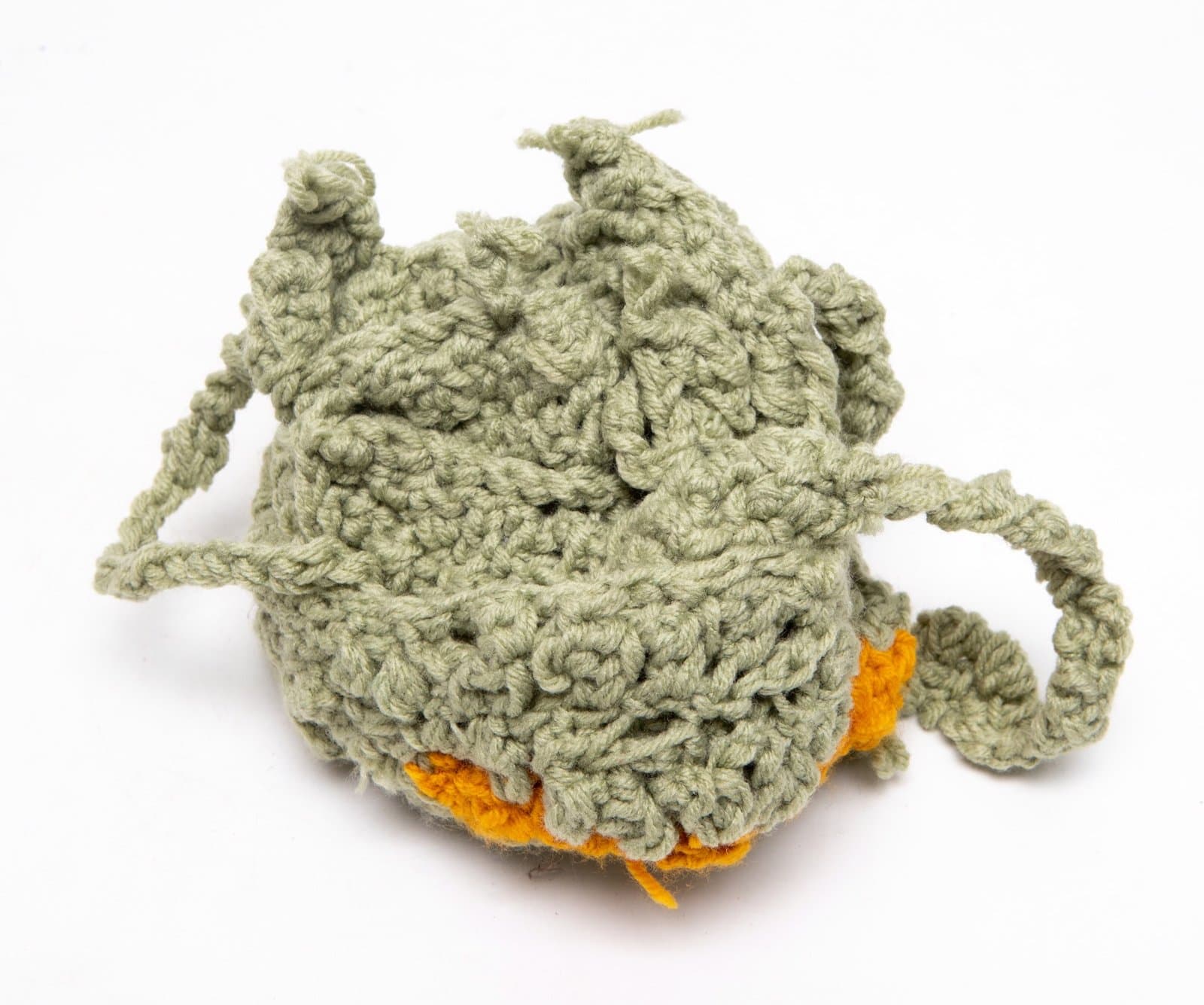 Crocheted sculpture in sage green yarn with orange accents, featuring irregular organic forms with extending tendrils