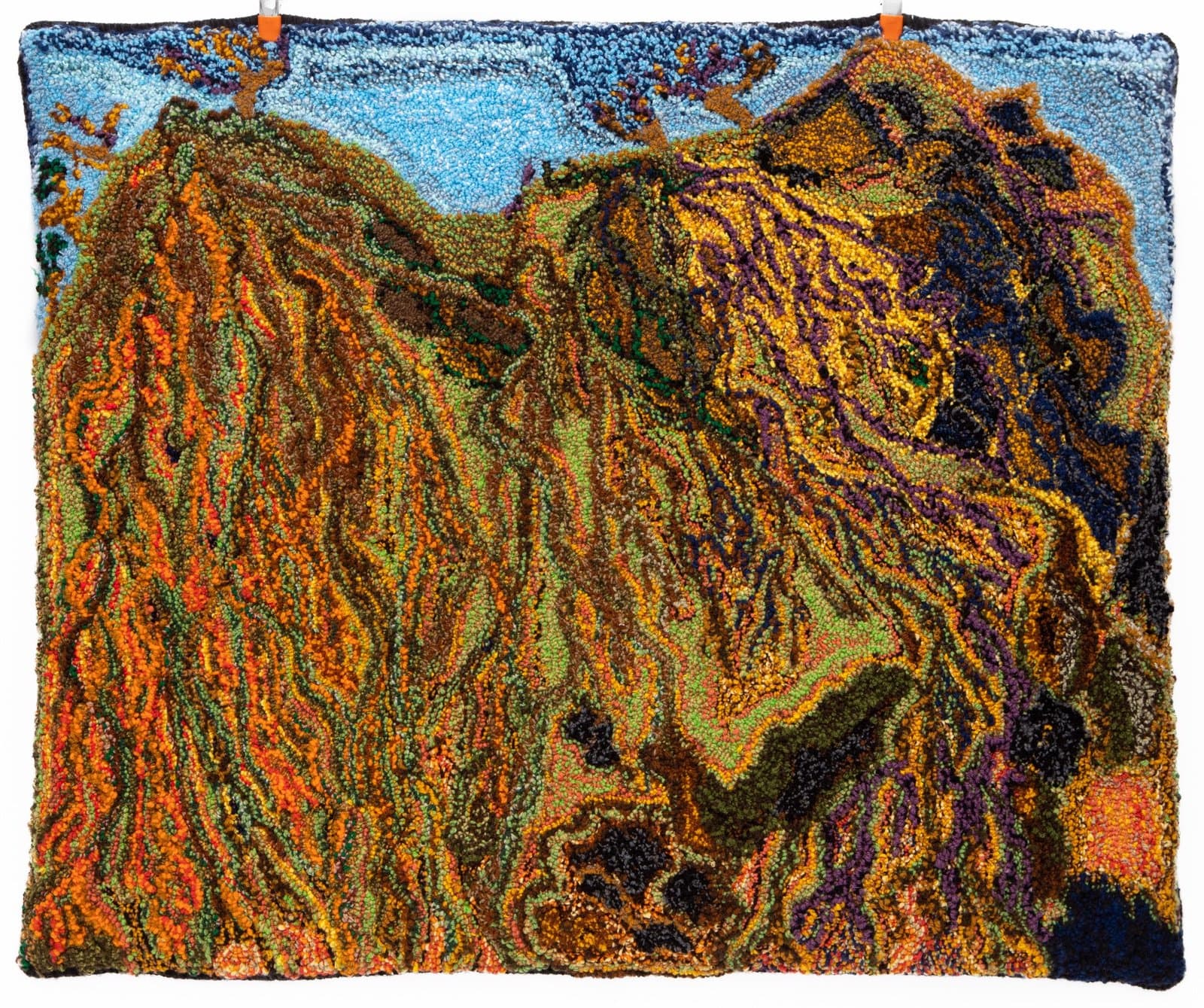 Hooked rug depicting mountainous landscape with flowing organic forms in warm earth tones against blue sky.