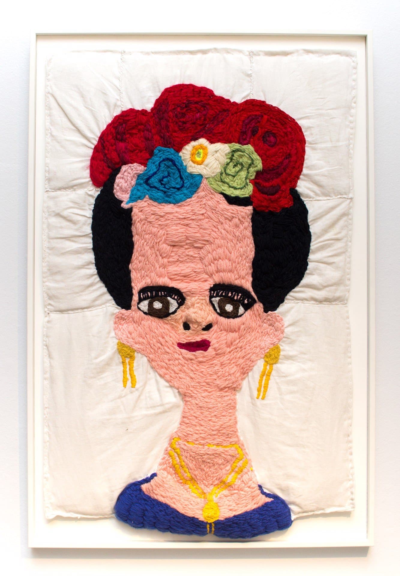 Embroidered textile portrait of figure with black hair, floral crown, and blue garment on white fabric background