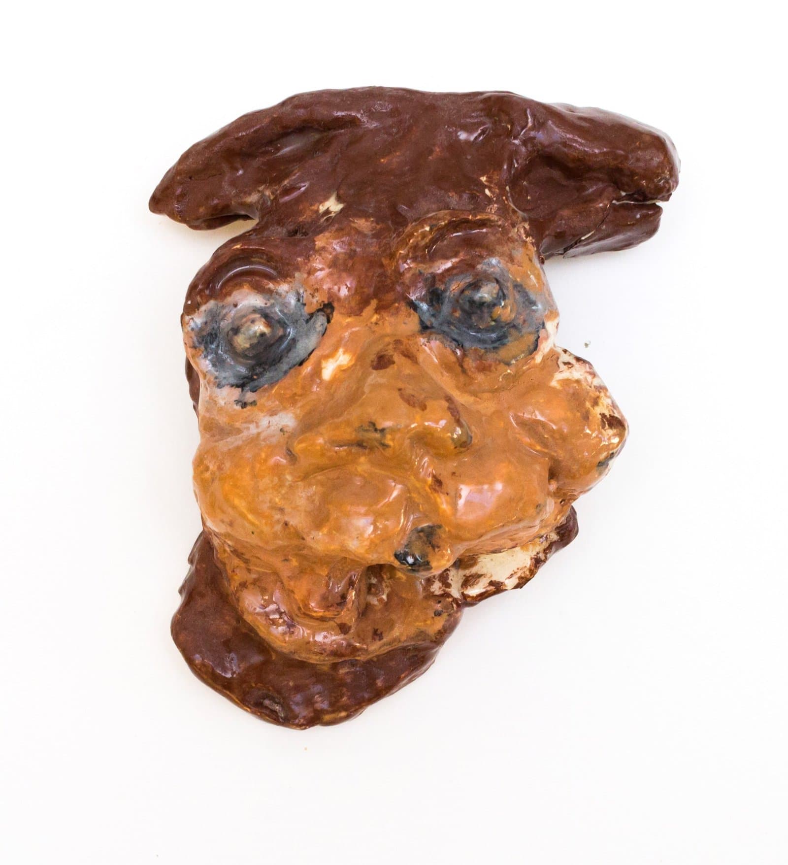 Ceramic sculpture of a distorted face with orange features and dark brown hair against white background